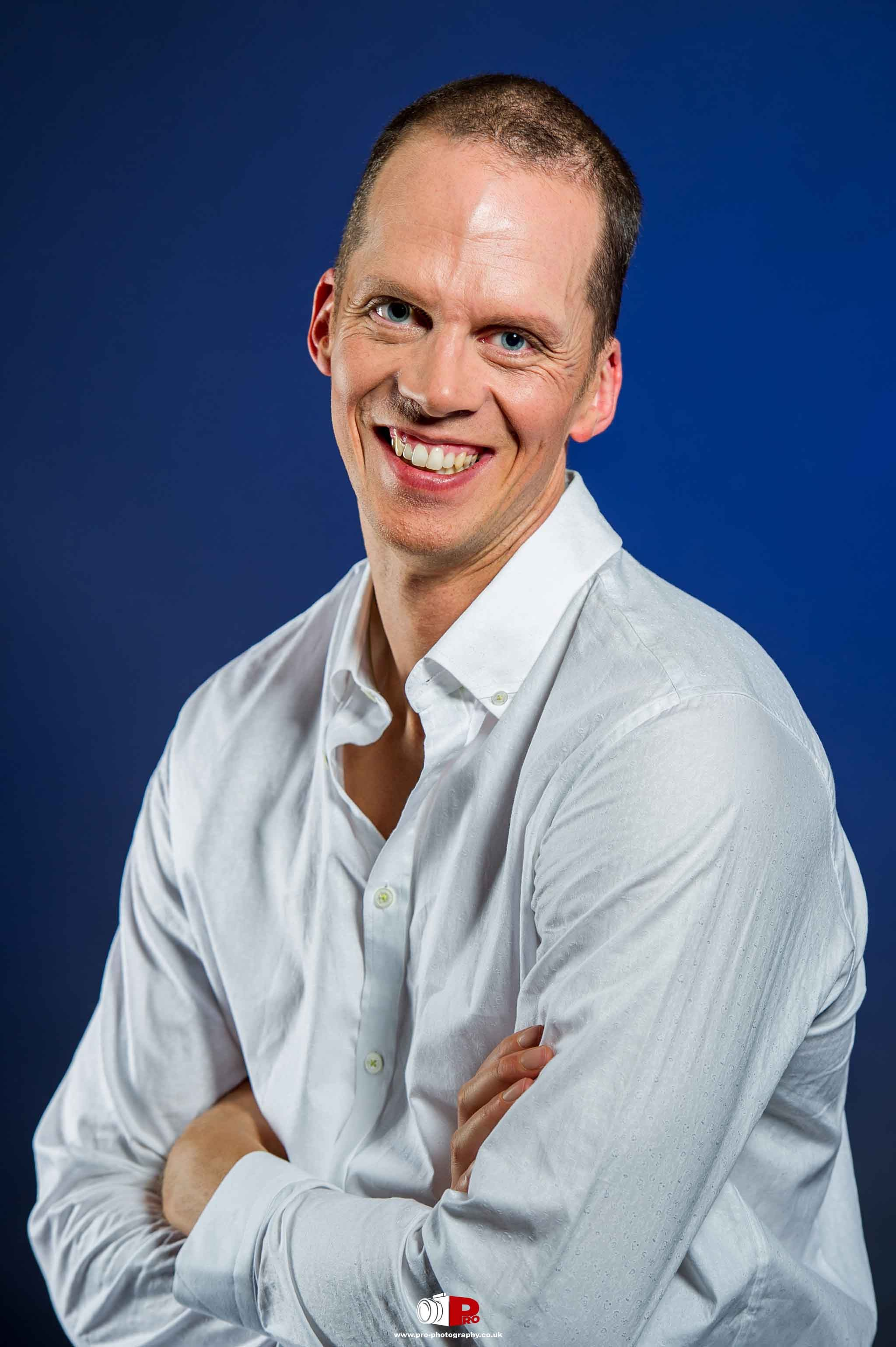 A man with a broad smile wearing a white shirt posing against a deep blue background.