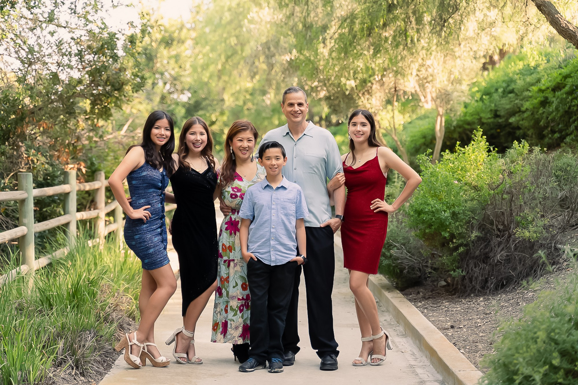 A family of six people smiling towards the camera while standing in beautiful light at a park in Orange County