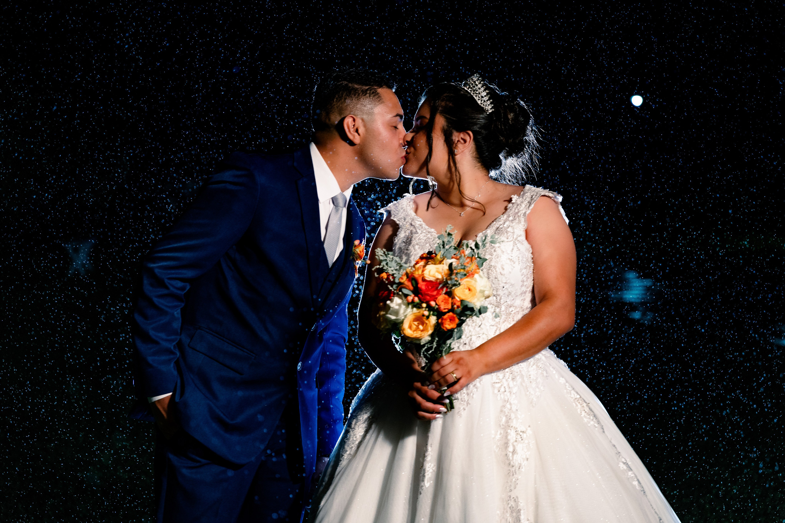Casal se beijando sob chuva com gotas iluminadas no fundo, cena intensa e cinematográfica.