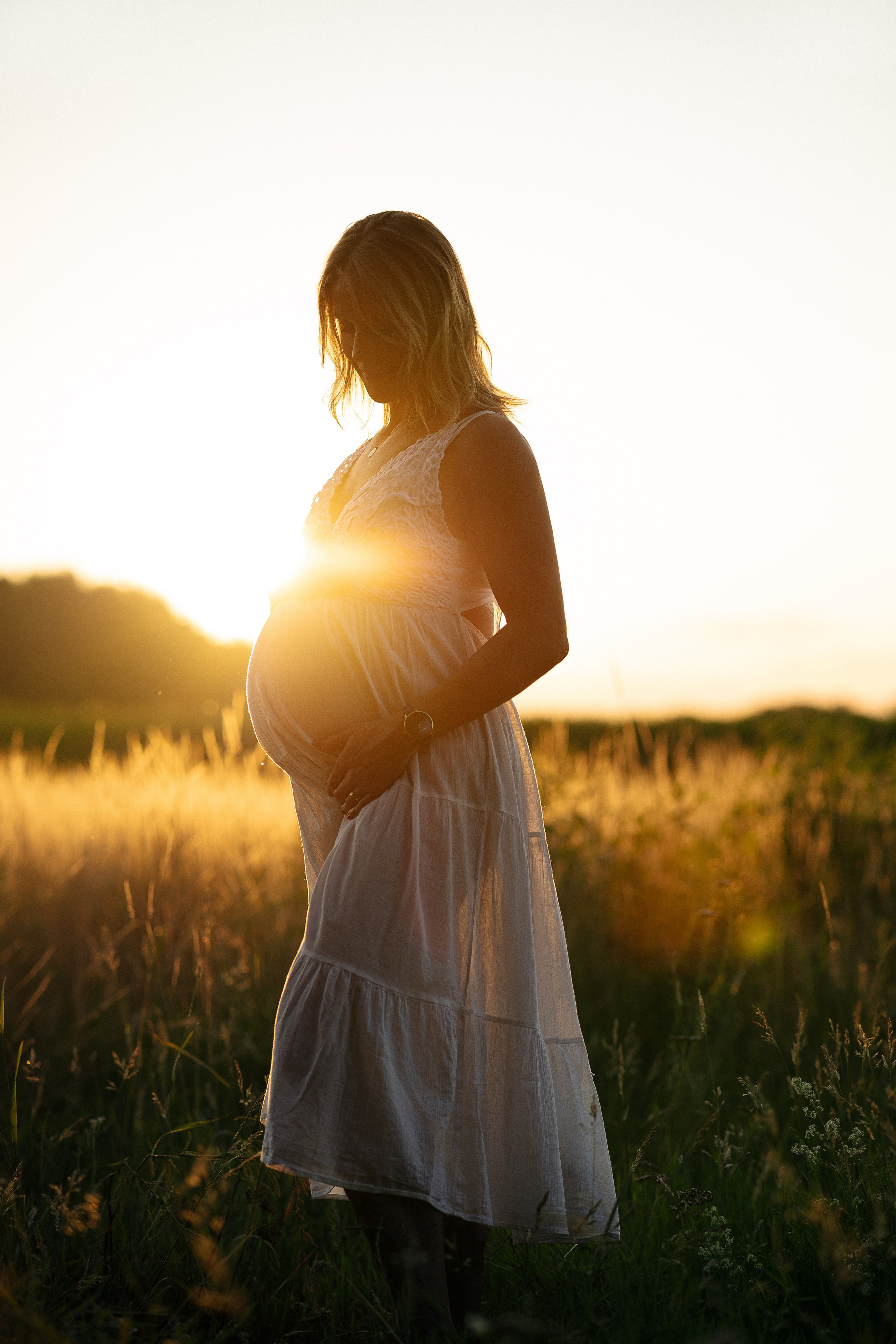 Schwangere Frau im warmen Gegenlicht der untergehenden Sonne während eines natürlichen Babybauchshootings im Feld.
