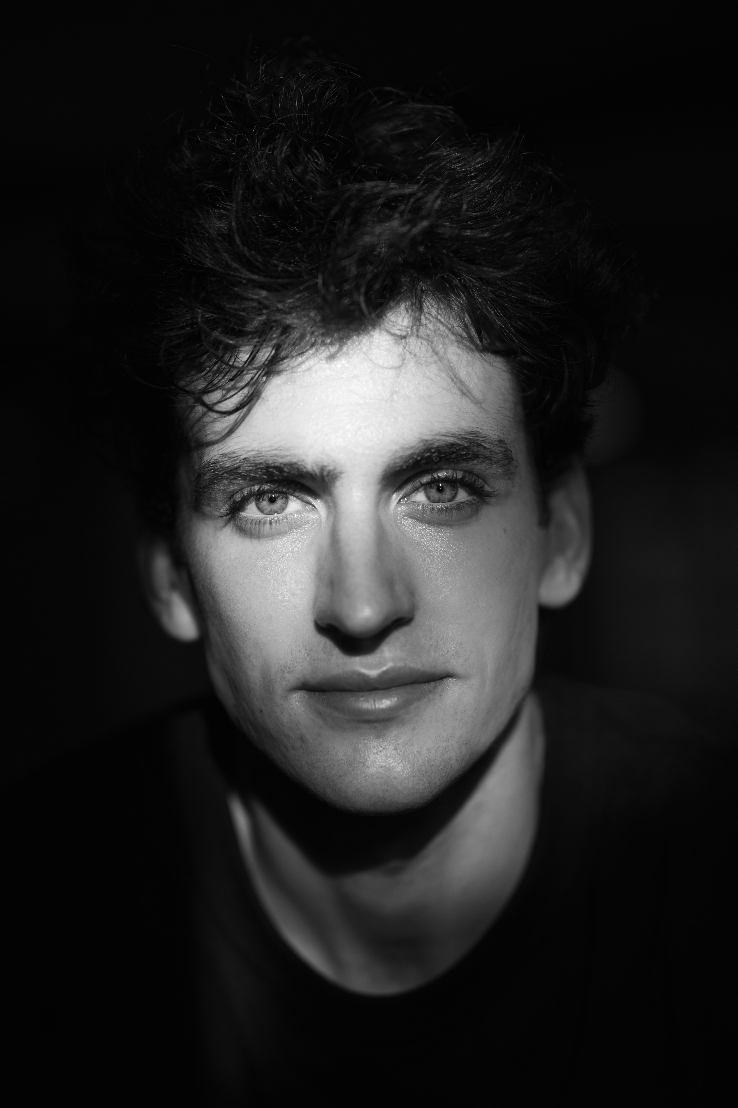 Black and white close-up of a young man’s face with a narrow beam of light across his eyes.