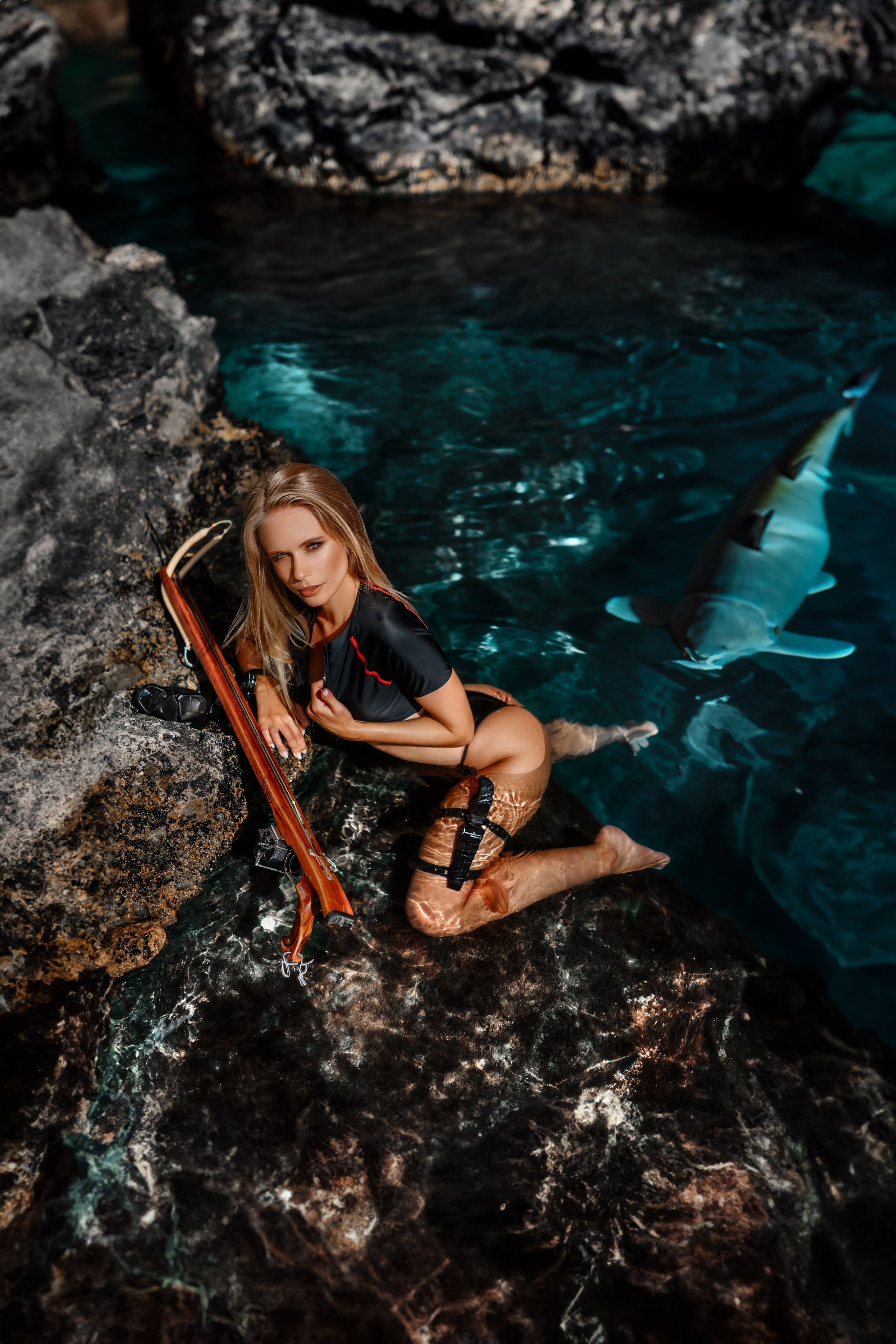 Set against the backdrop of breathtaking oceanfront cliffs, a female fashion photoshoot of the highest caliber commences. A young woman, dressed in a sleek diving bikini and carrying an underwater hunting rifle, stands in the water, poised for a submerged pursuit of her quarry
