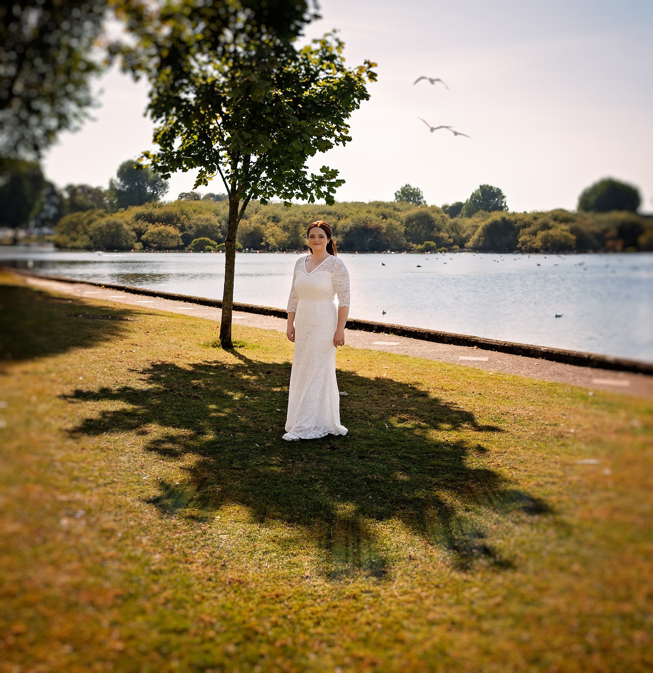 Bride and groom posing together hand-in-hand along a sunny lakeside path. Fine art wedding photography serving Cork.