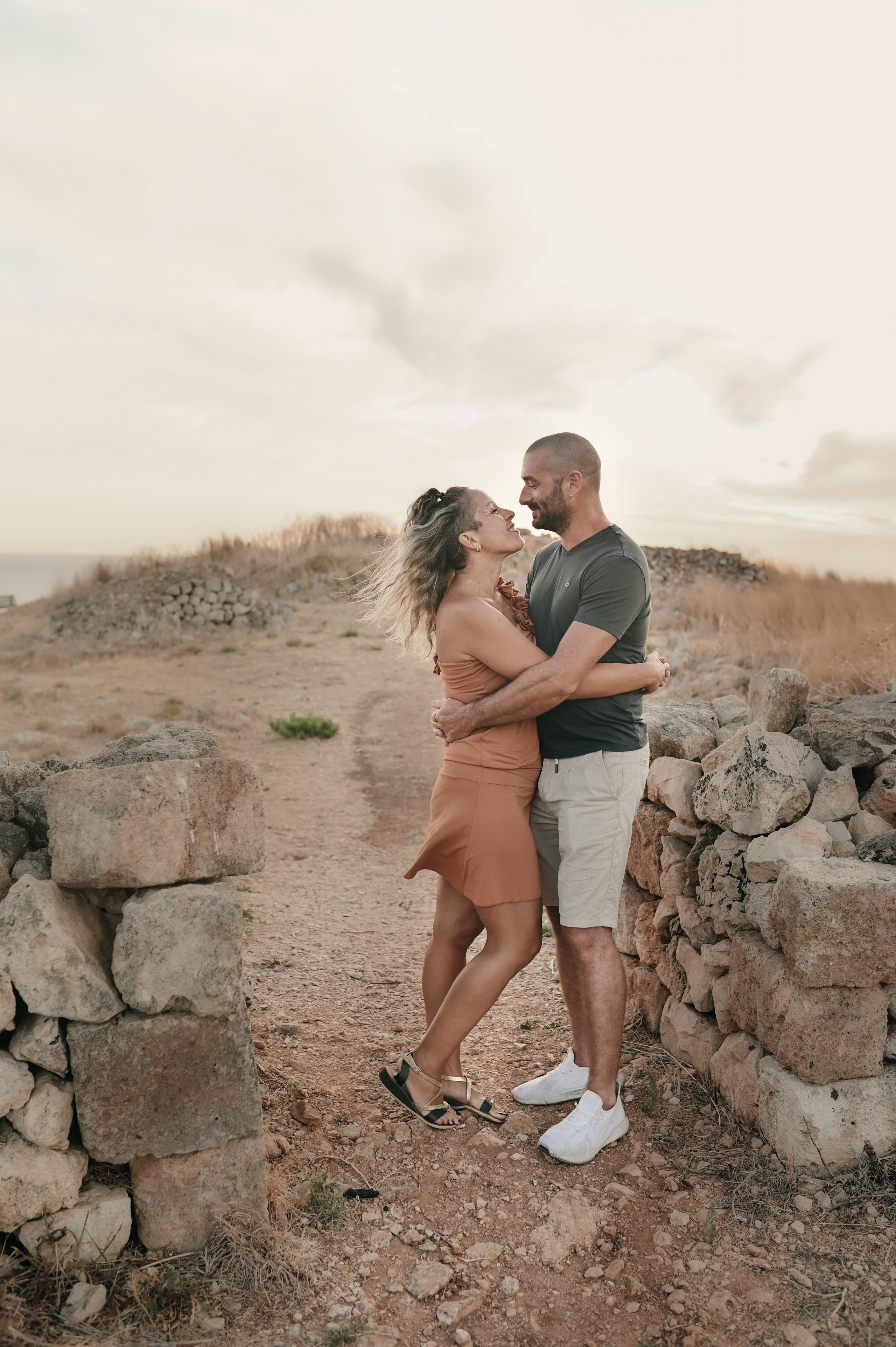 Couple embracing in a rocky, sun-drenched landscape — a romantic moment during a couple photoshoot in southern Italy.