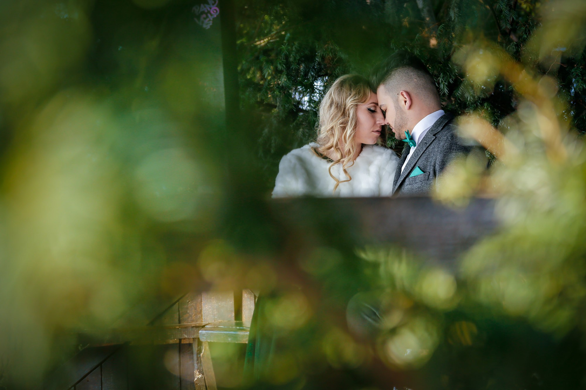 Close-up portrait of the smiling newlyweds beautifully framed by green leaves, creating a fresh and natural visual effect.