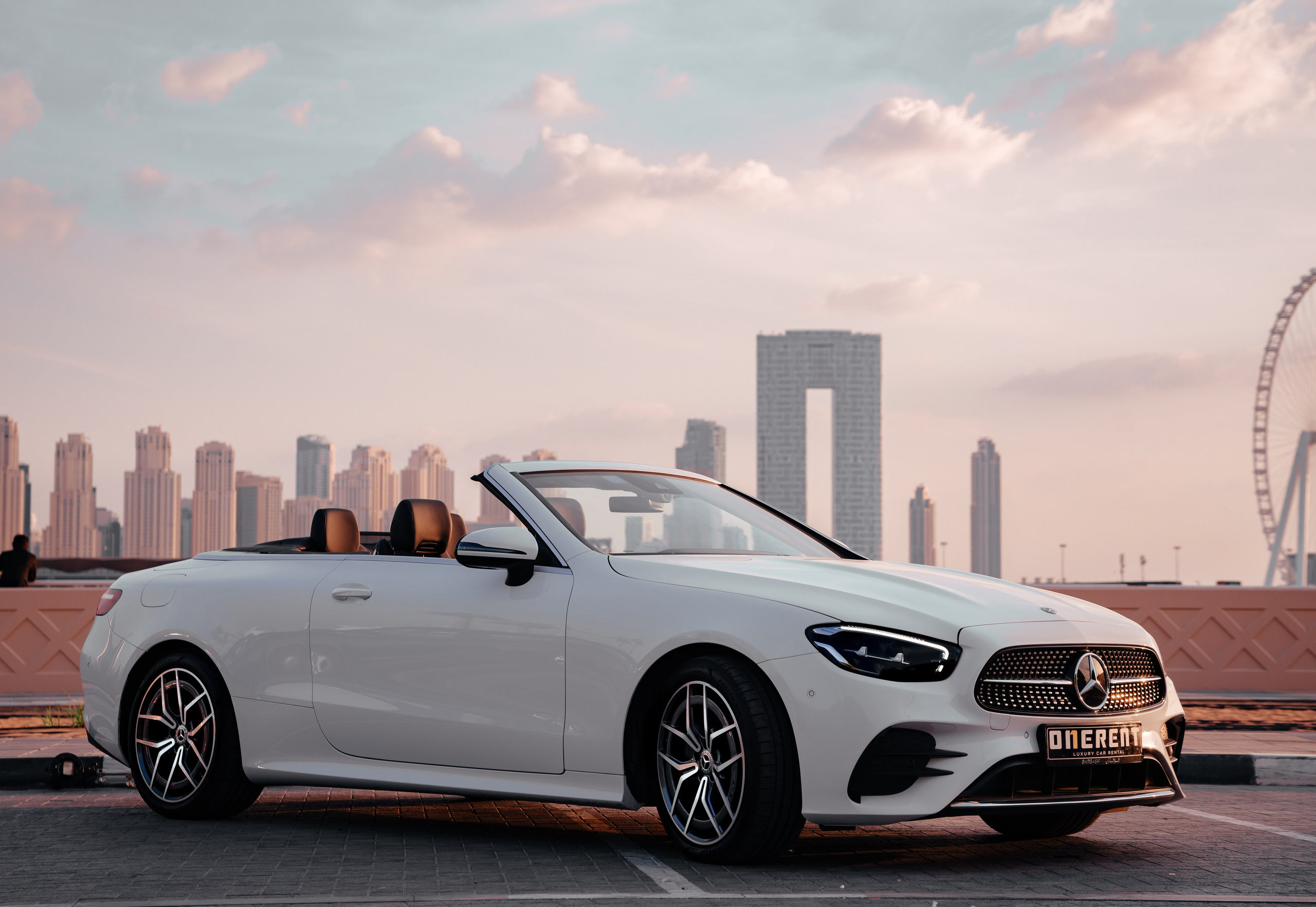 A white Mercedes with a stunning view of Dubai’s sunset landscape in the background.