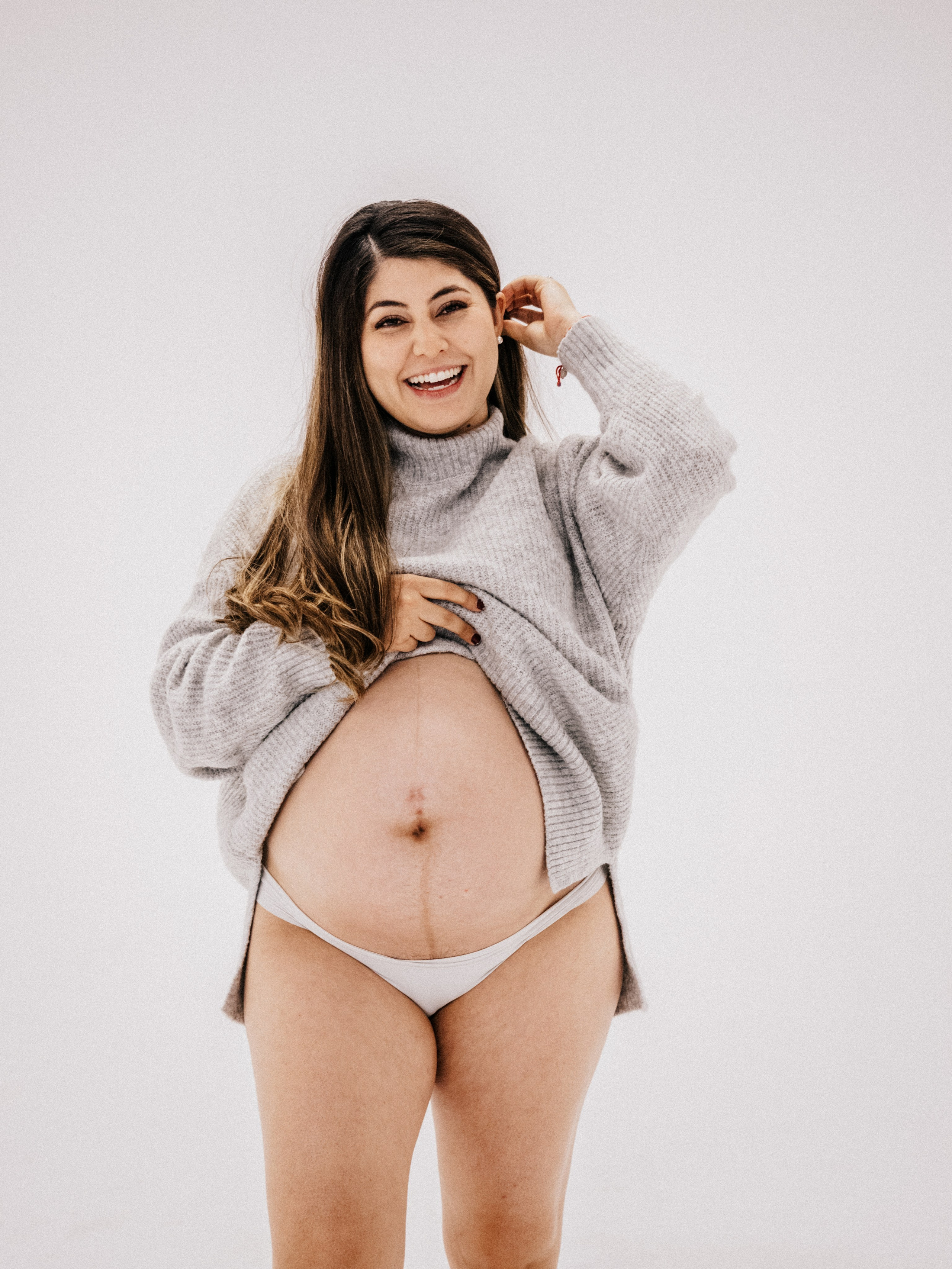Pregnant woman smiling in front of a white background in a studio in Montreal.