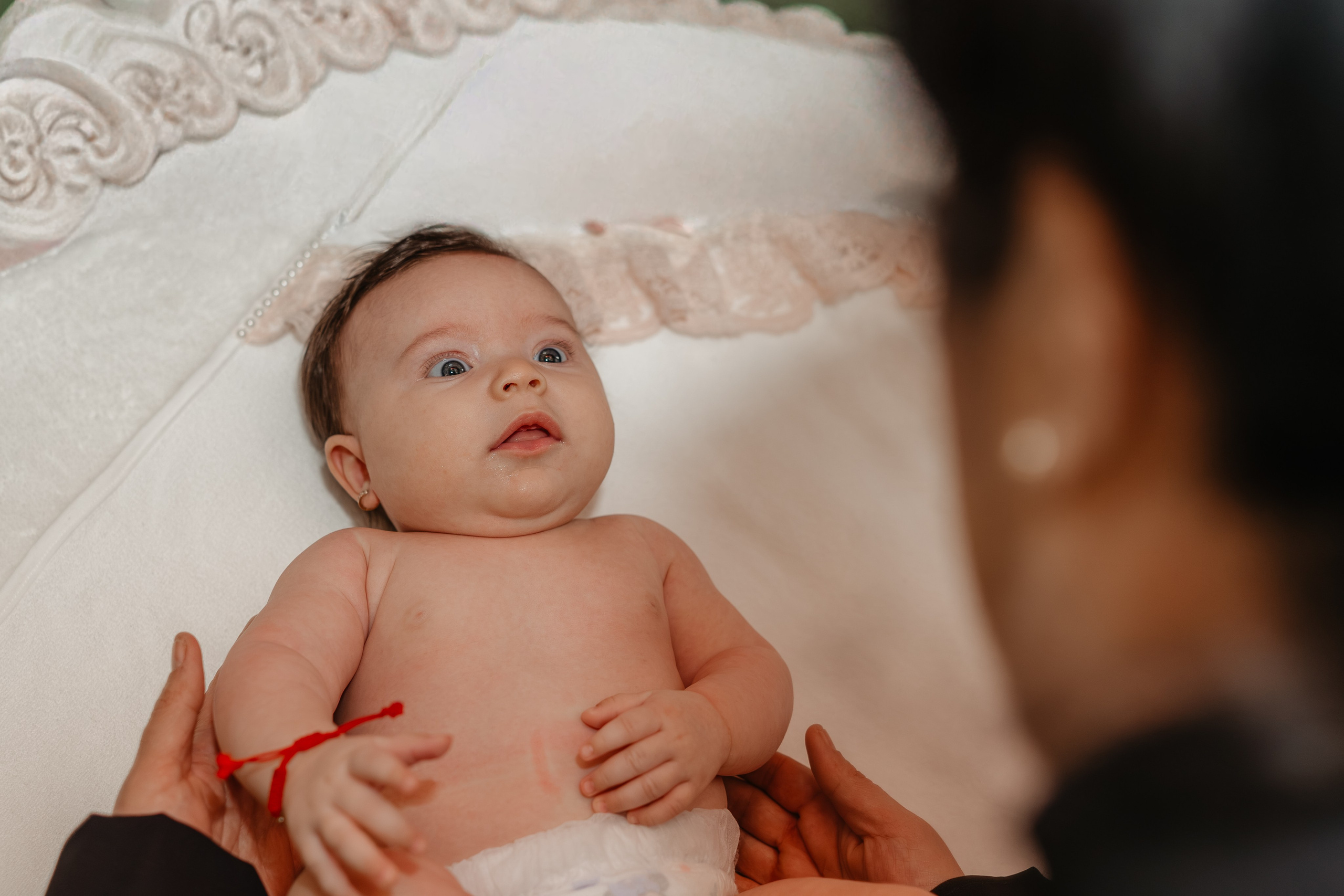 Fetița Eveline Maria, aproape dezbrăcată pentru scăldătoarea sfântă, stă pe masă și privește uimită și plină de încredere în sus, spre nașa ei. Un moment intim și plin de tandrețe dinaintea scăldării la botez.