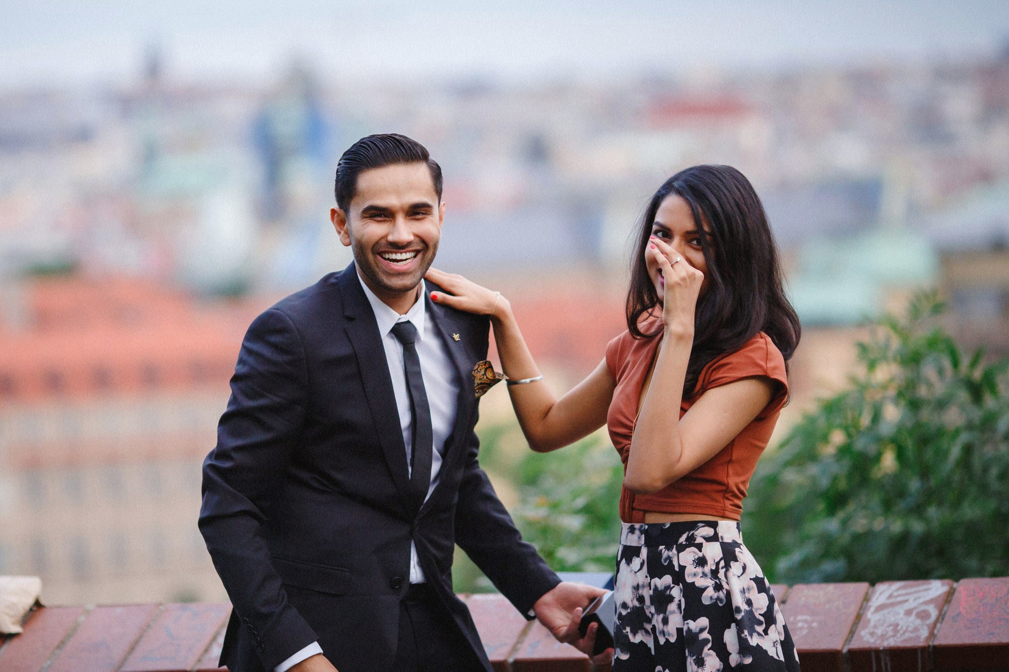 Man laughing as woman covers face in surprise shortly after Prague marriage proposal.