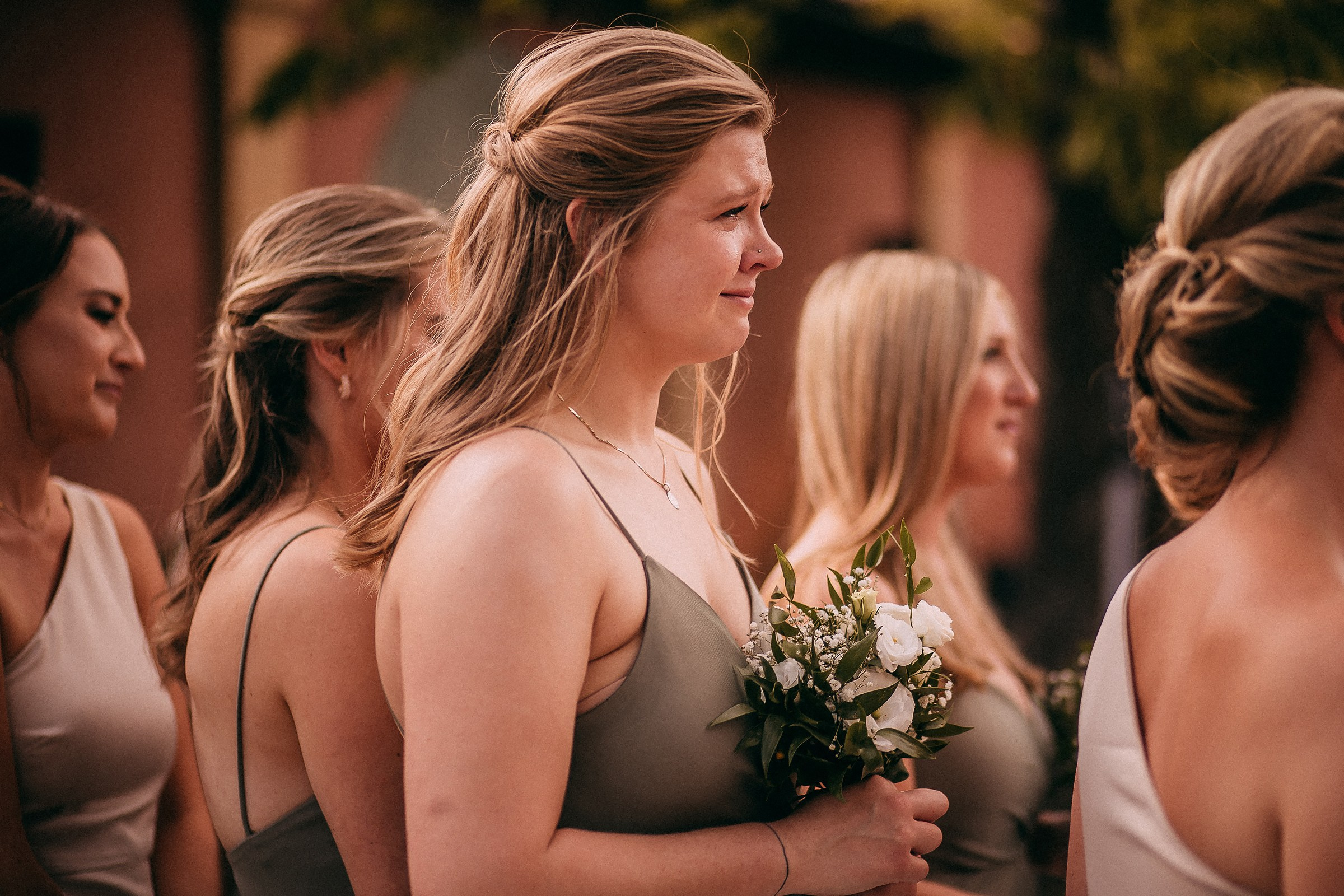 A close-up of a bridesmaid with tears in her eyes, holding a bouquet of white flowers during the emotional wedding ceremony.