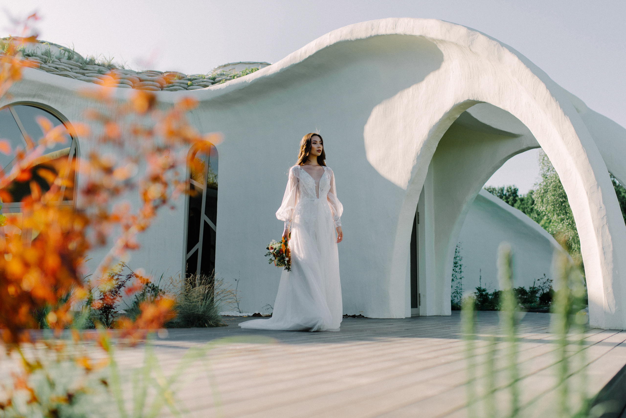 Bride in a white wedding dress with a bouquet of flowers on the background of a white fairy-tale house.
