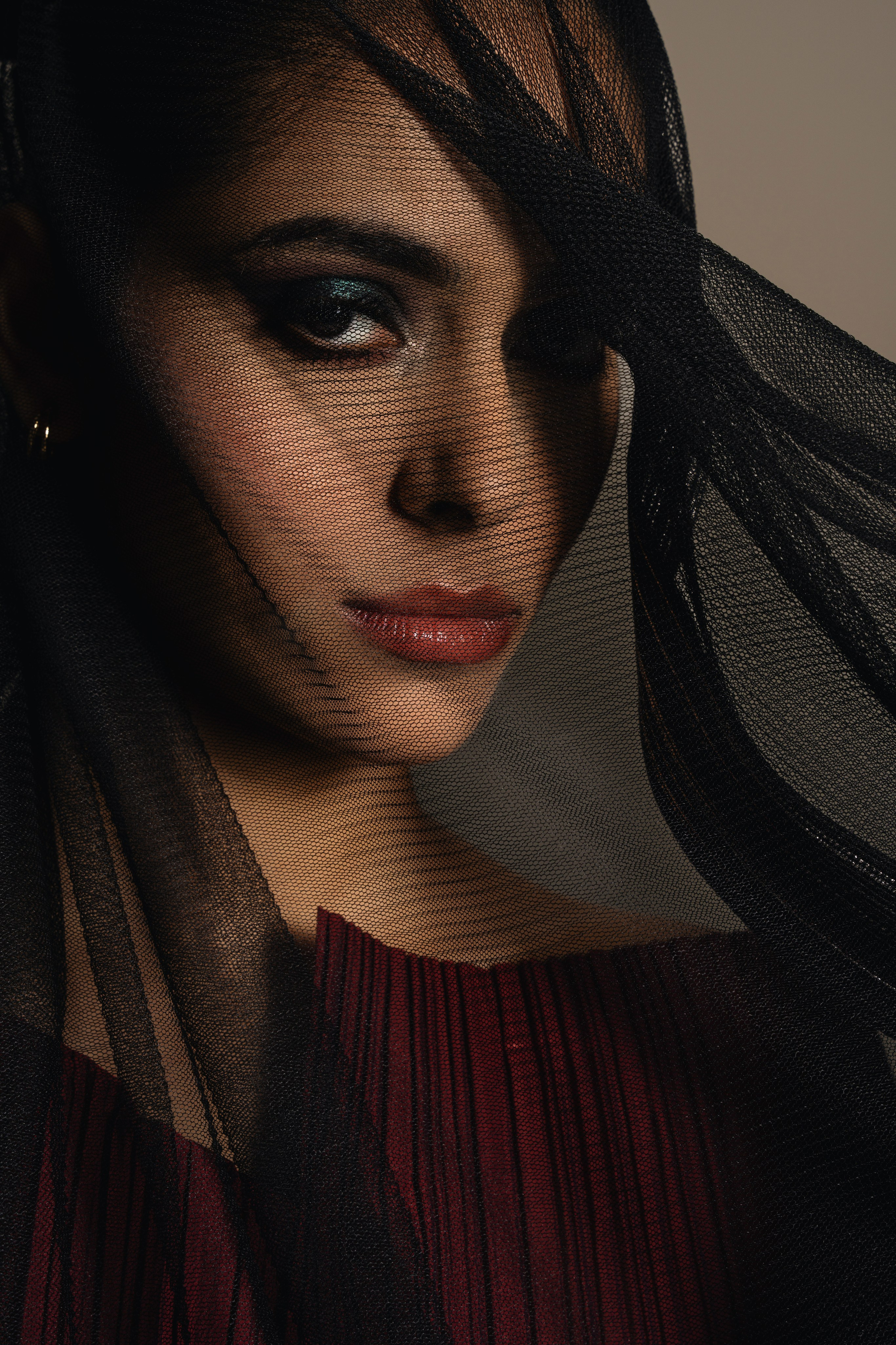 Beauty portrait of a woman partially framed by a dark veil, photographed in soft light with a cinematic editorial mood.