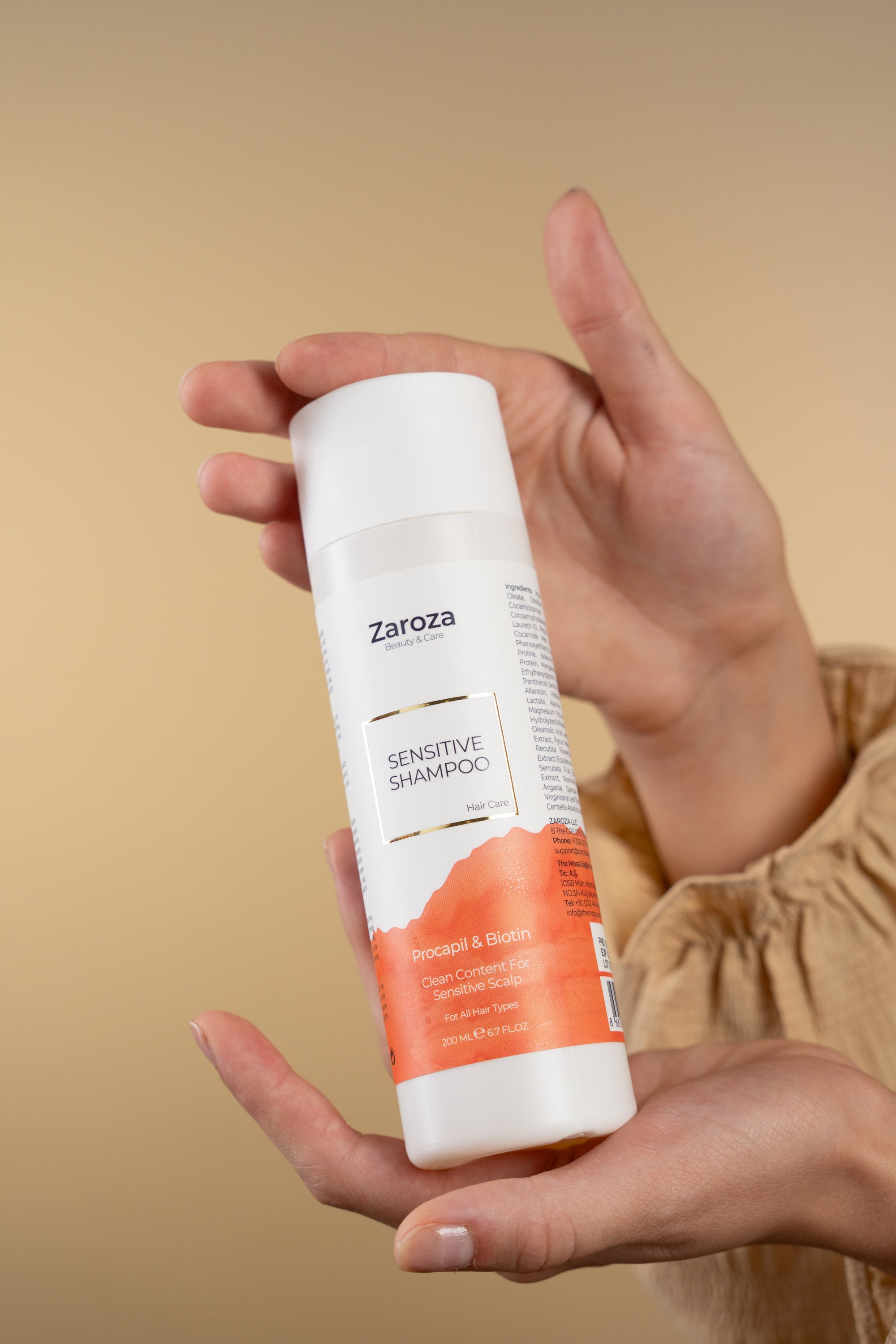 Zarozanın Sensitive Shampoo şüşəsi, bej fonda iki əlin arasında təqdim olunan məhsul fotoşəkili.