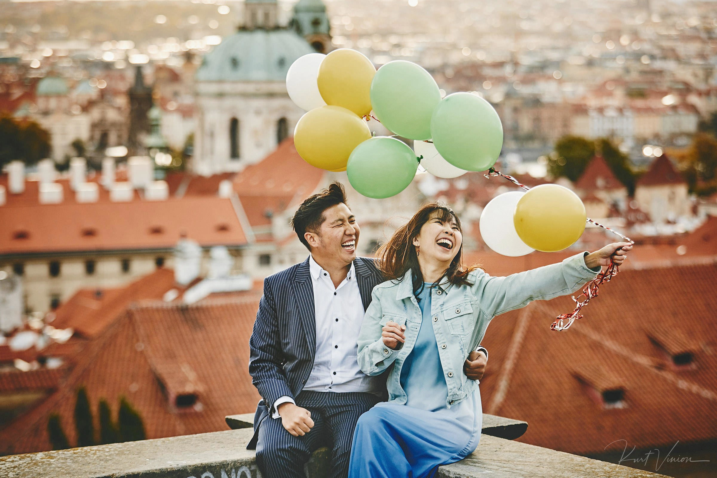Asian woman smiling with balloons laughing as partner laughs above Prague city.