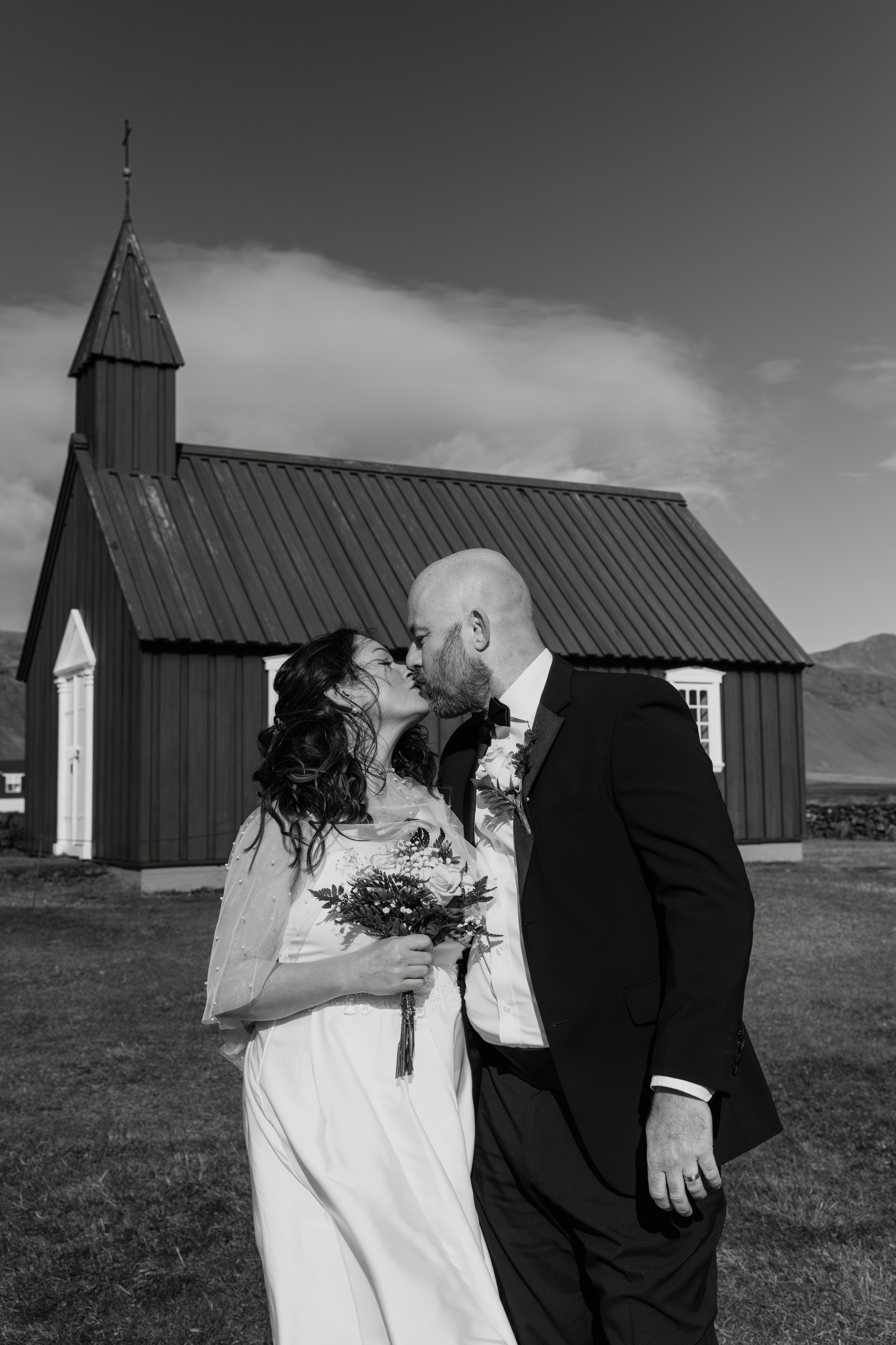 Bride and groom standing in front of the iconic black Búðakirkja, with dramatic Icelandic skies above.