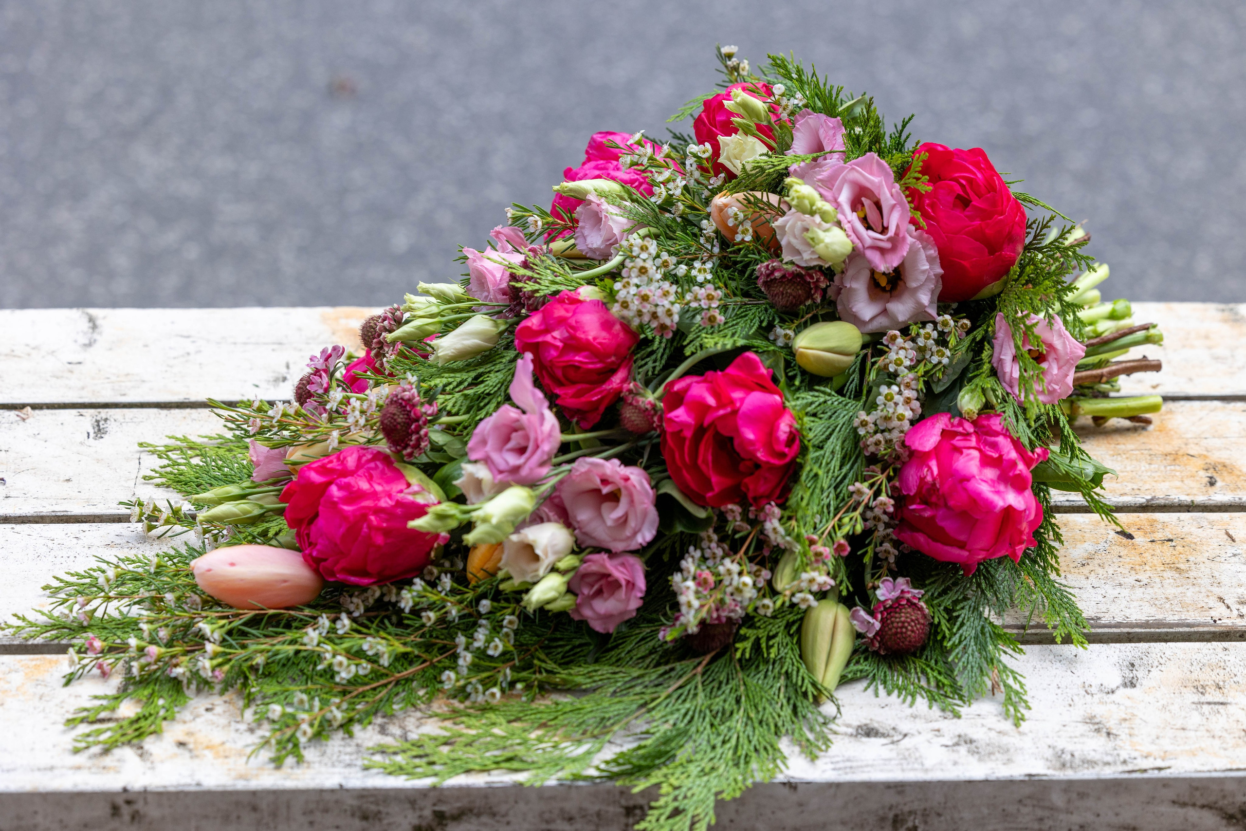 En let og luftig bårebuket, hvor blomsterne er bundet i liggende position. Hver blomst fremhæves smukt med varierede grønt imellem. Bårebuketten er bundet med pink, hvilket lyser ethvert kirkegulv i enhver sæson.