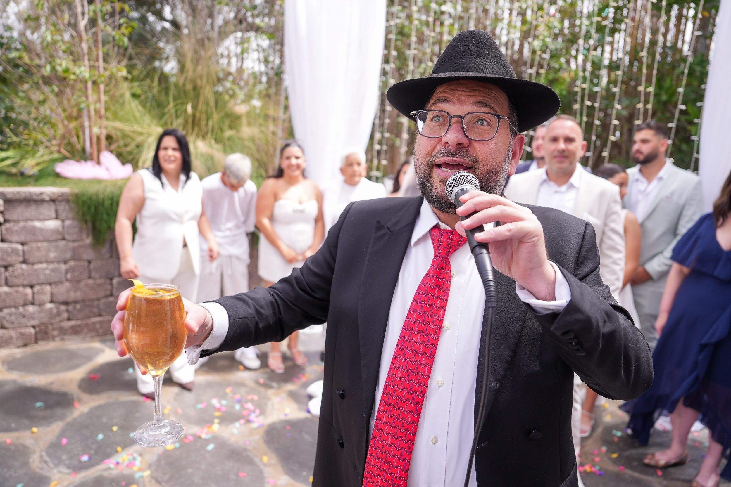 A rabbi holds a wine glass and speaks during a Jewish wedding ceremony