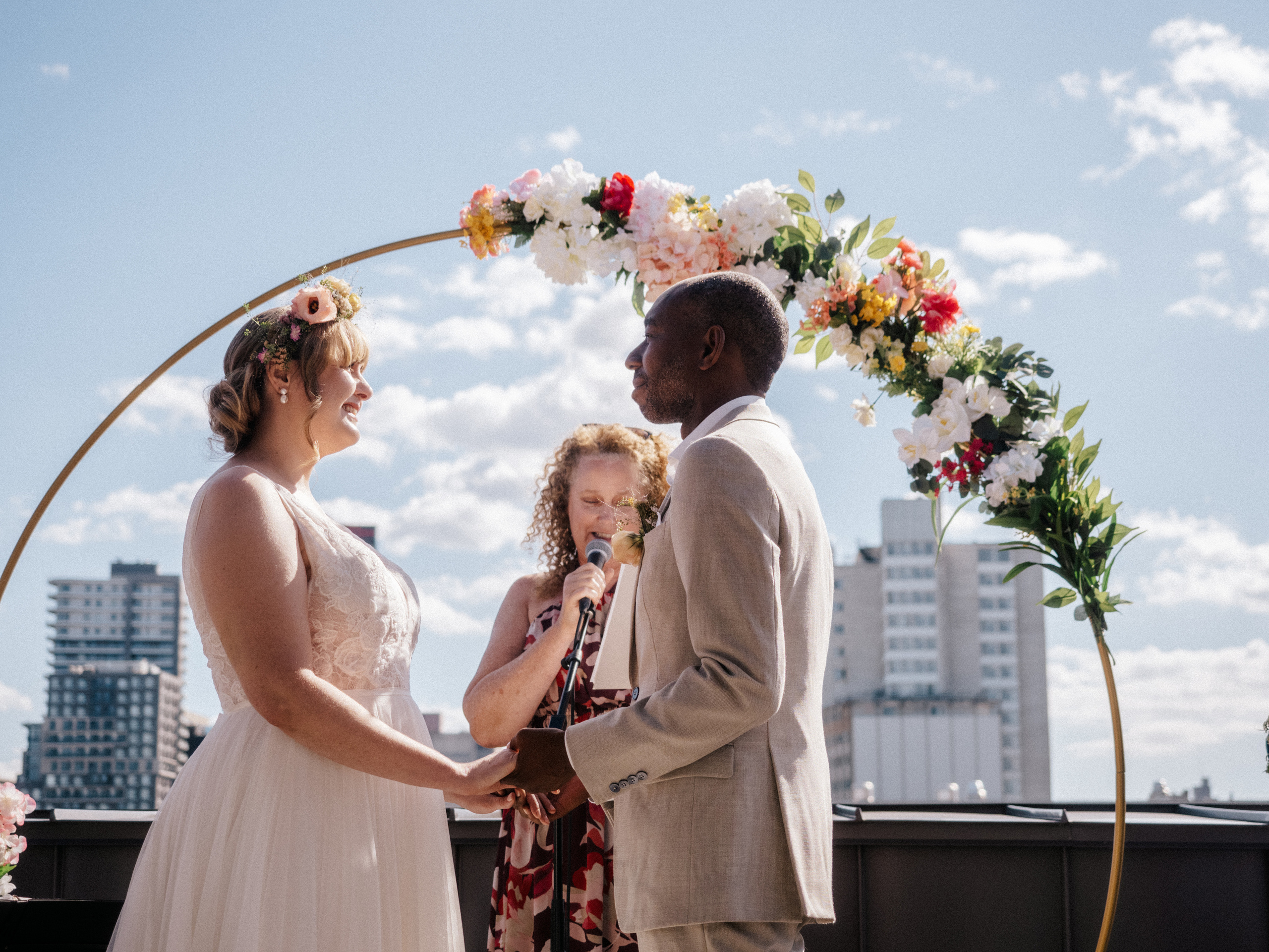 Couple in front of floral arch with blue sky in the back on rooftop terrace in Montreal, Canada.