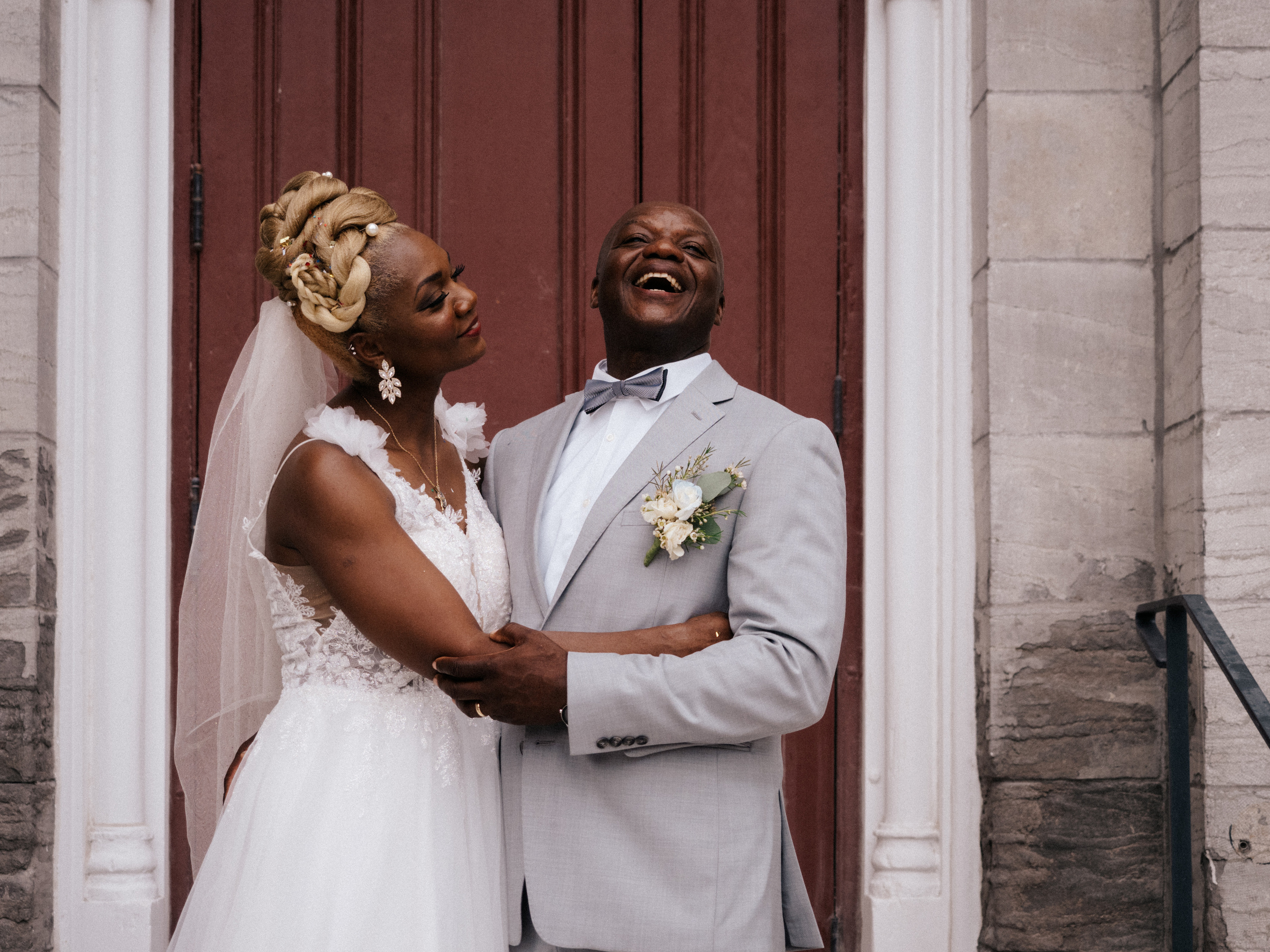 Bride and groom laughing in front of red door.