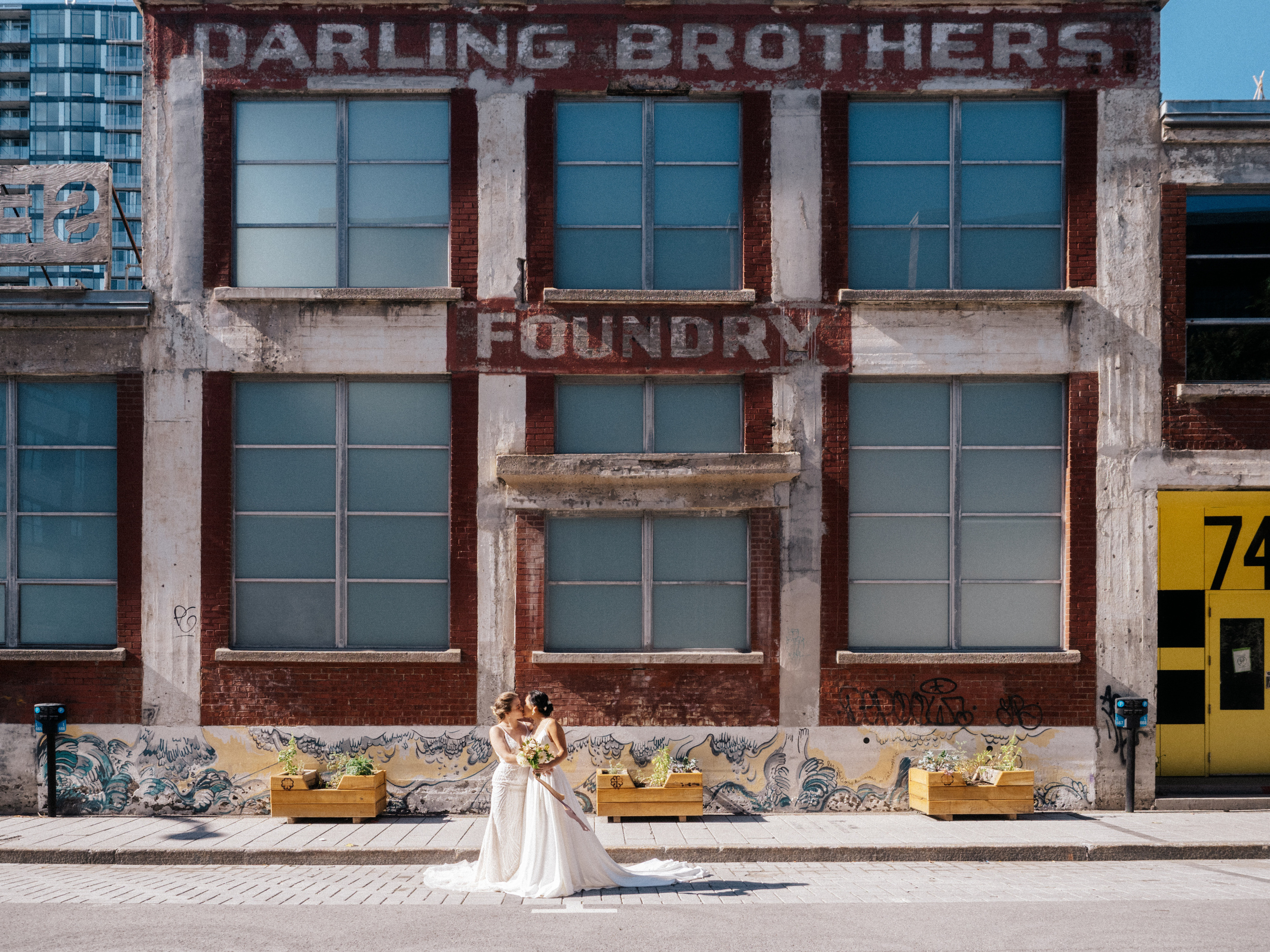 Lesbian couple in wedding attire kissing in front of factory building downtown Montreal, Canada. 