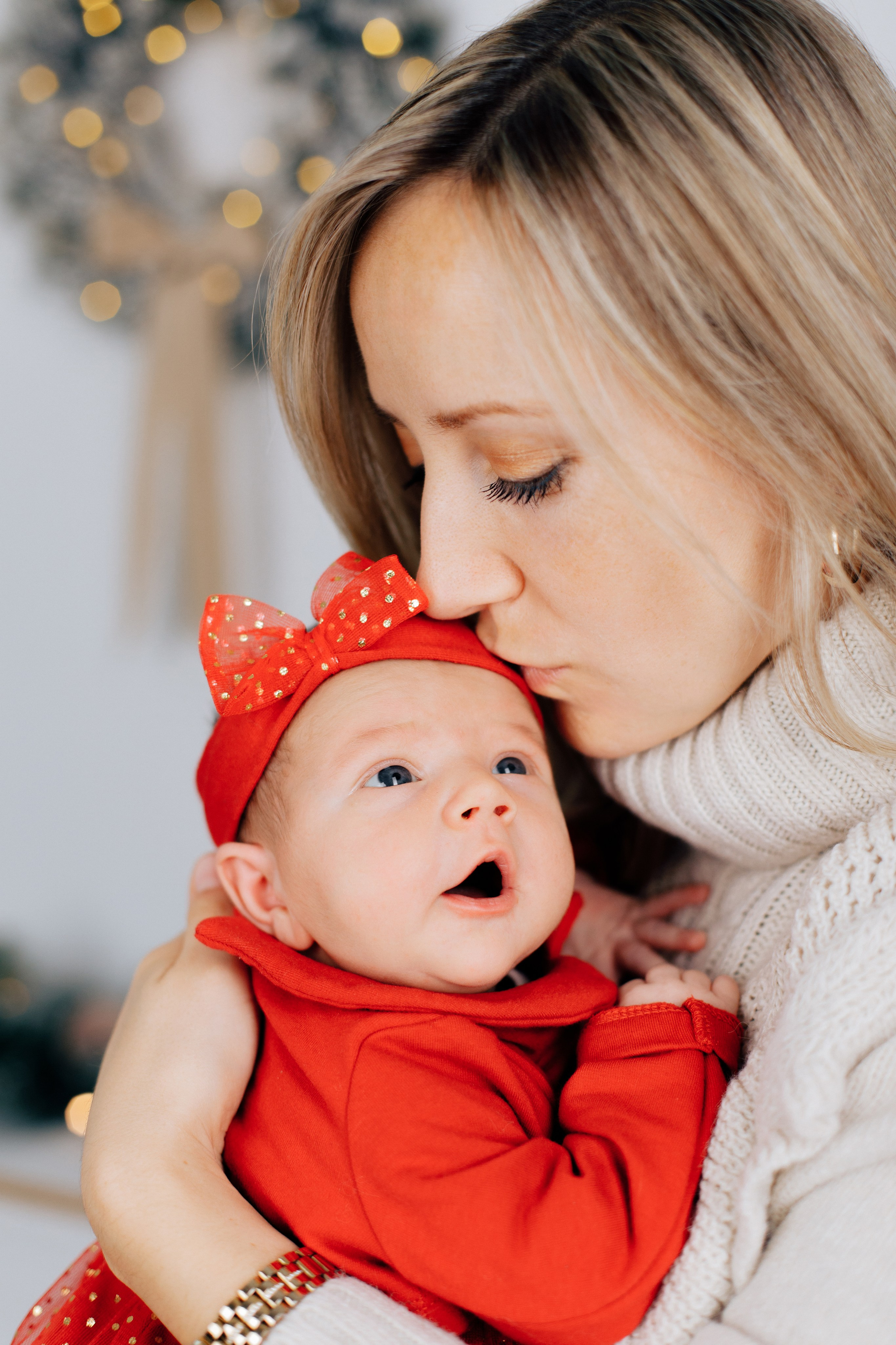 Mutter küsst ihr Baby, das im Weihnachtsoutfit gekleidet ist.