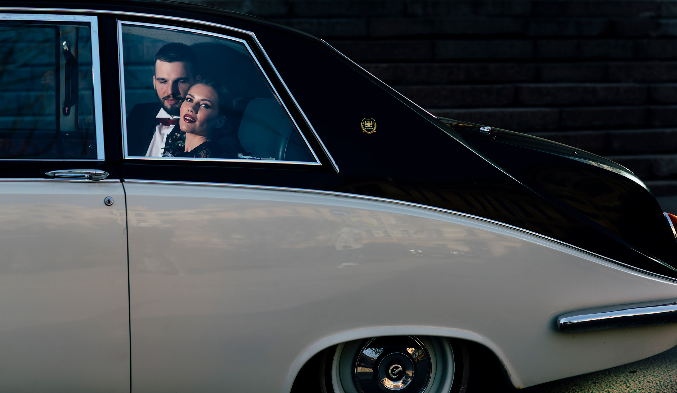dramatic portrait of bride and groom sitting an a premium black and white car