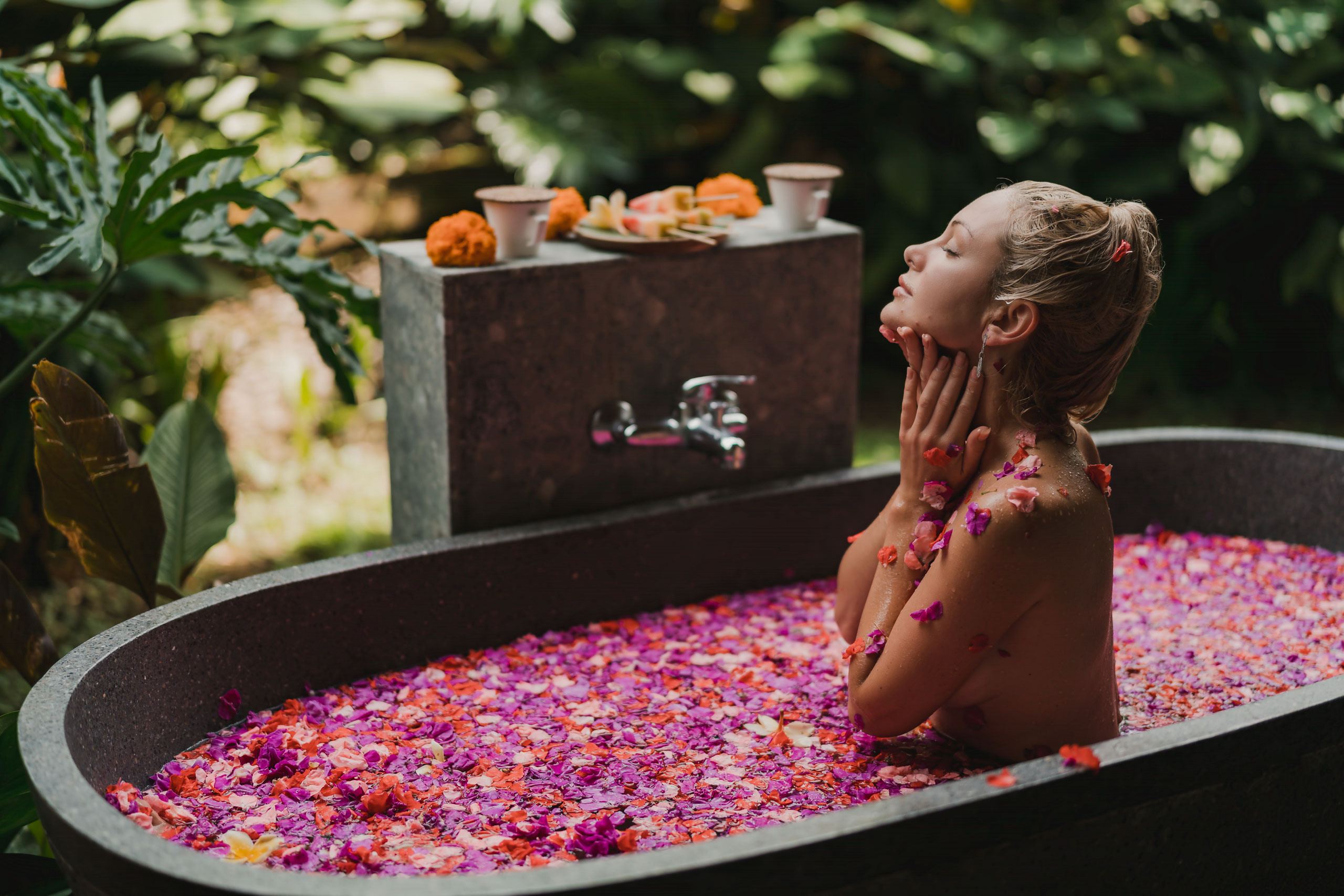 naked lady taking bath full of purple and pink flowers with the jungles on a background