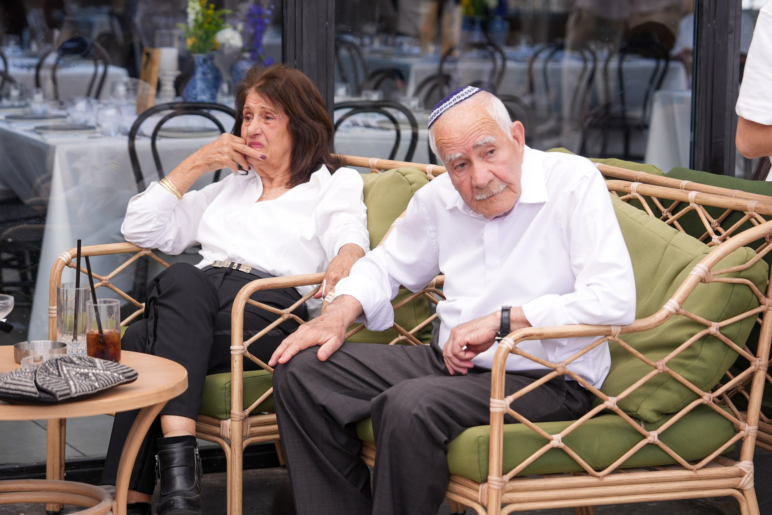 An older couple relaxes together on an outdoor sofa during the wedding reception