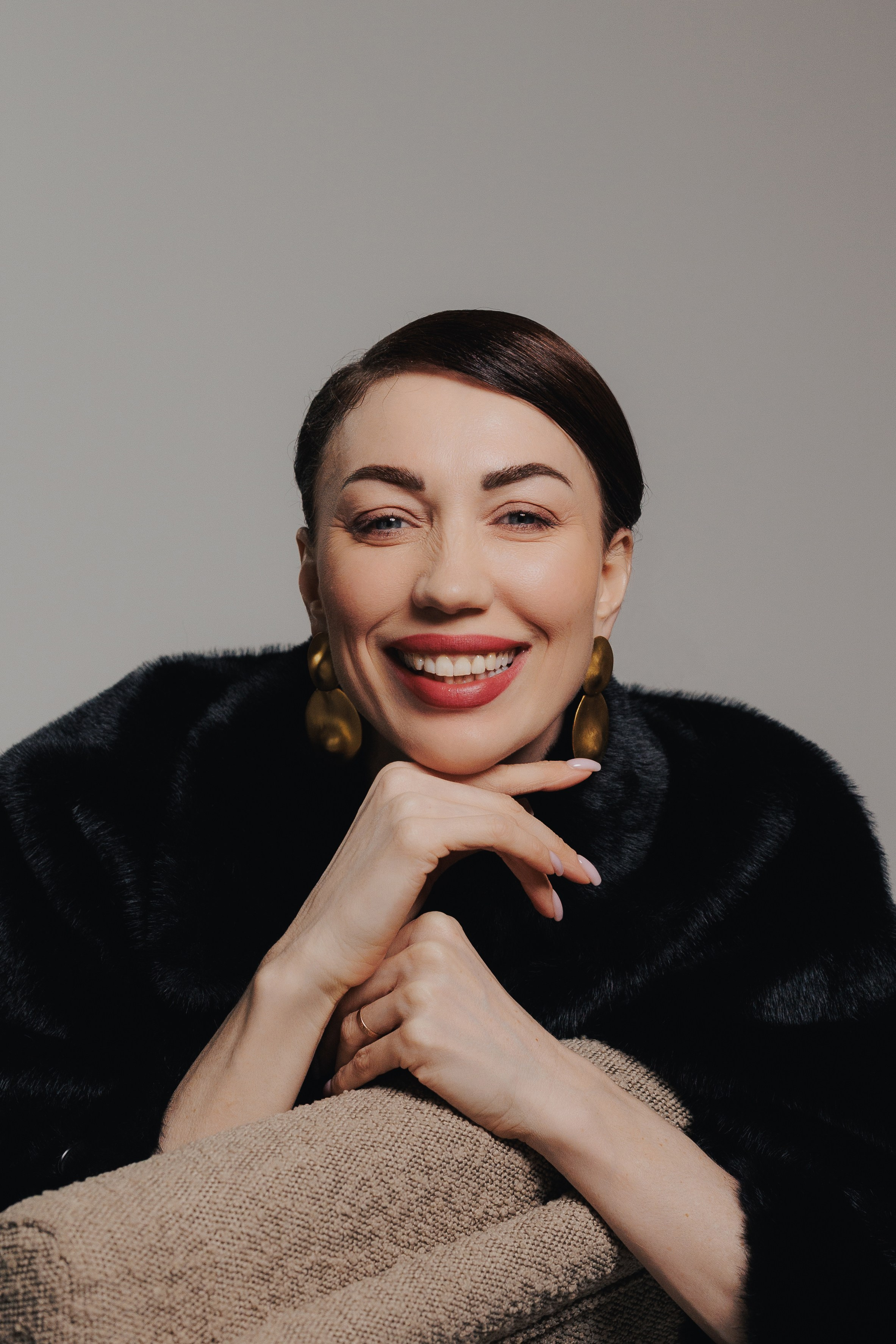 Elegant studio portrait of a woman with slick hair and natural makeup, resting her chin on her hands, photographed in soft editorial lighting by Leipzig portrait photographer Kristina Kozheltsova. Элегантный студийный портрет женщины с гладко уложенными волосами и натуральным макияжем, снятый в мягком редакционном свете фотографом Кристиной Кожельцовой.