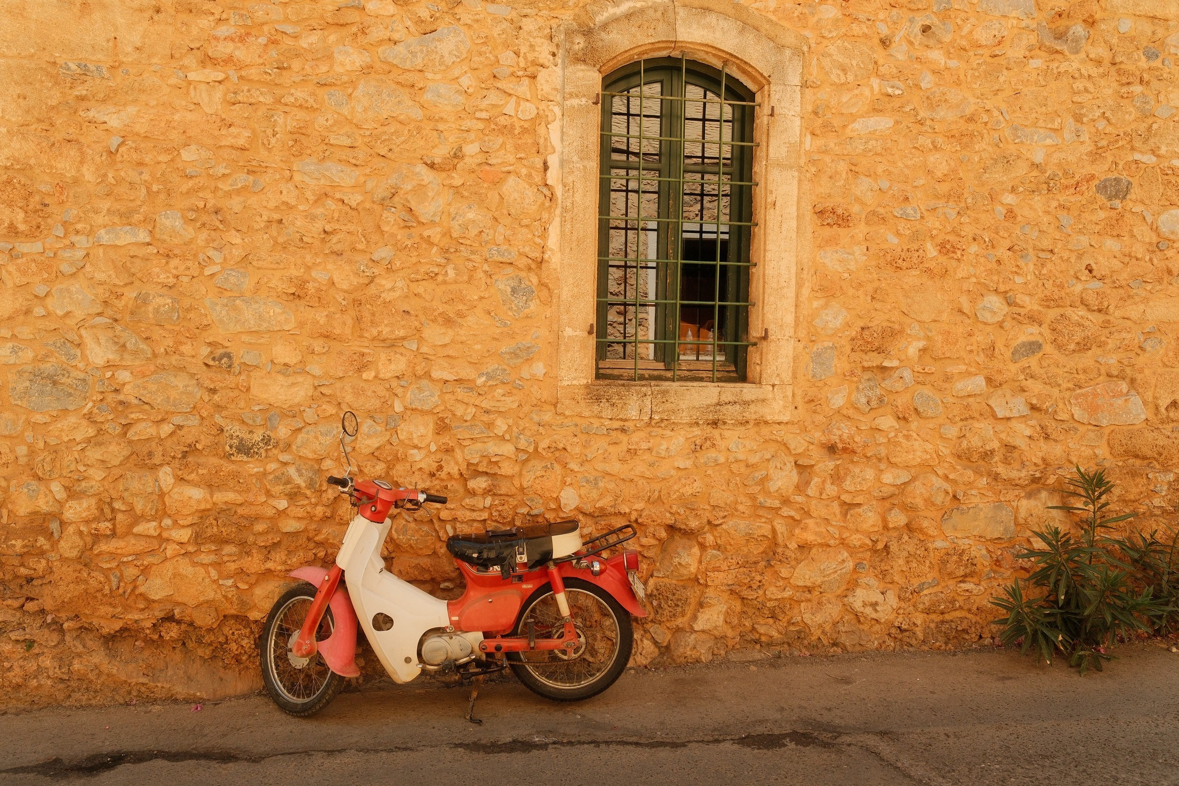 Red moped against a stone wall in Malia, Crete, photographed with a Fujifilm X-H2S.