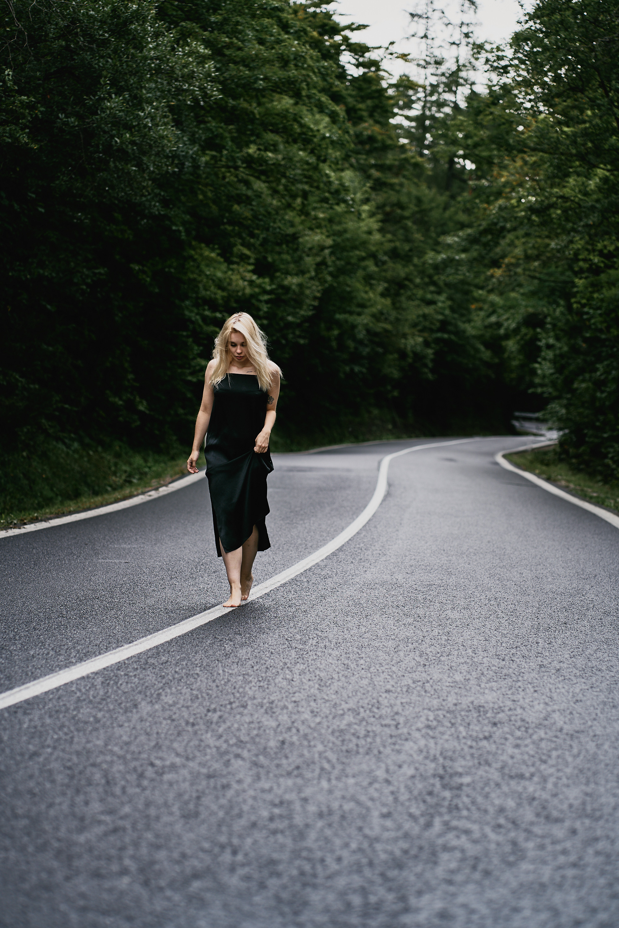 A woman walking alone on a deserted road framed by dense green forest, symbolizing solitude and freedom.