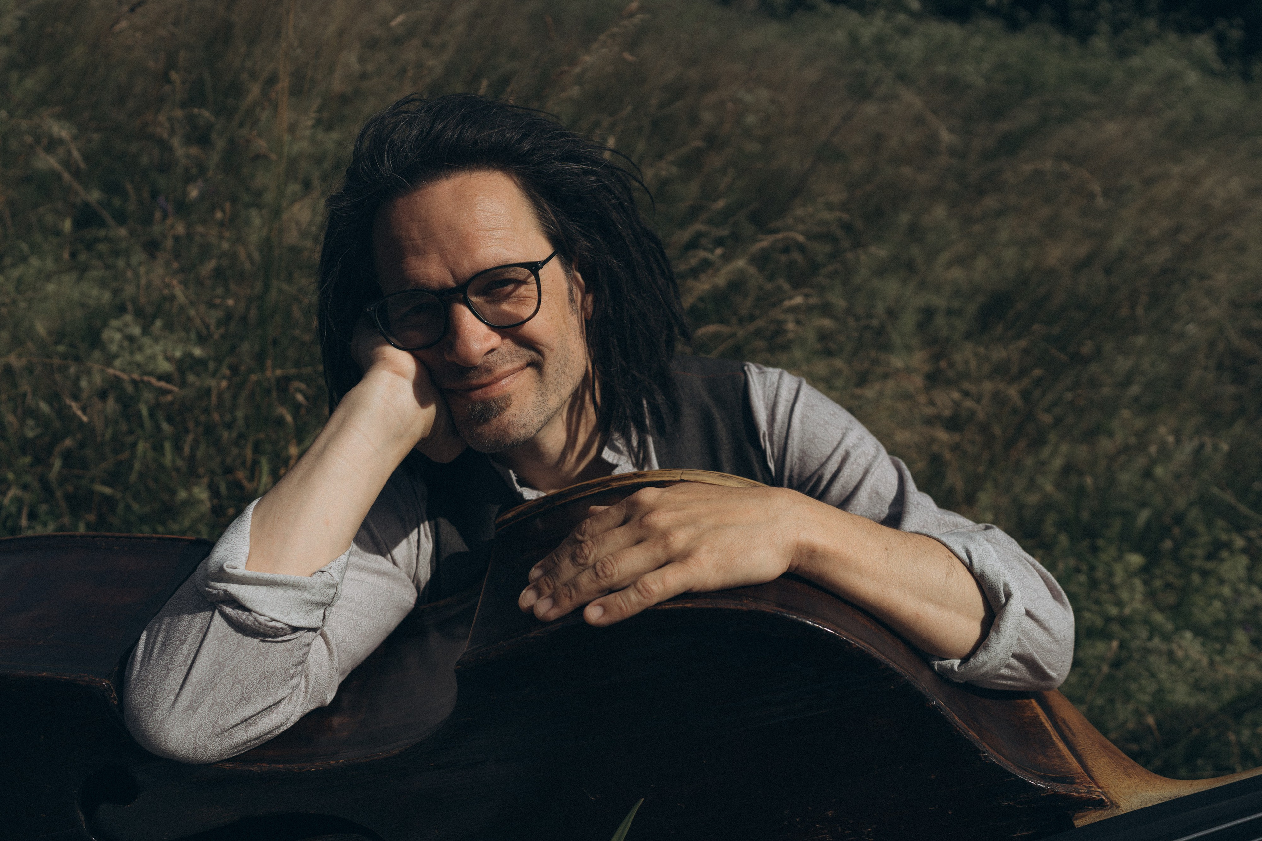 Musiker lehnt entspannt am Kontrabass, Sommerlicht