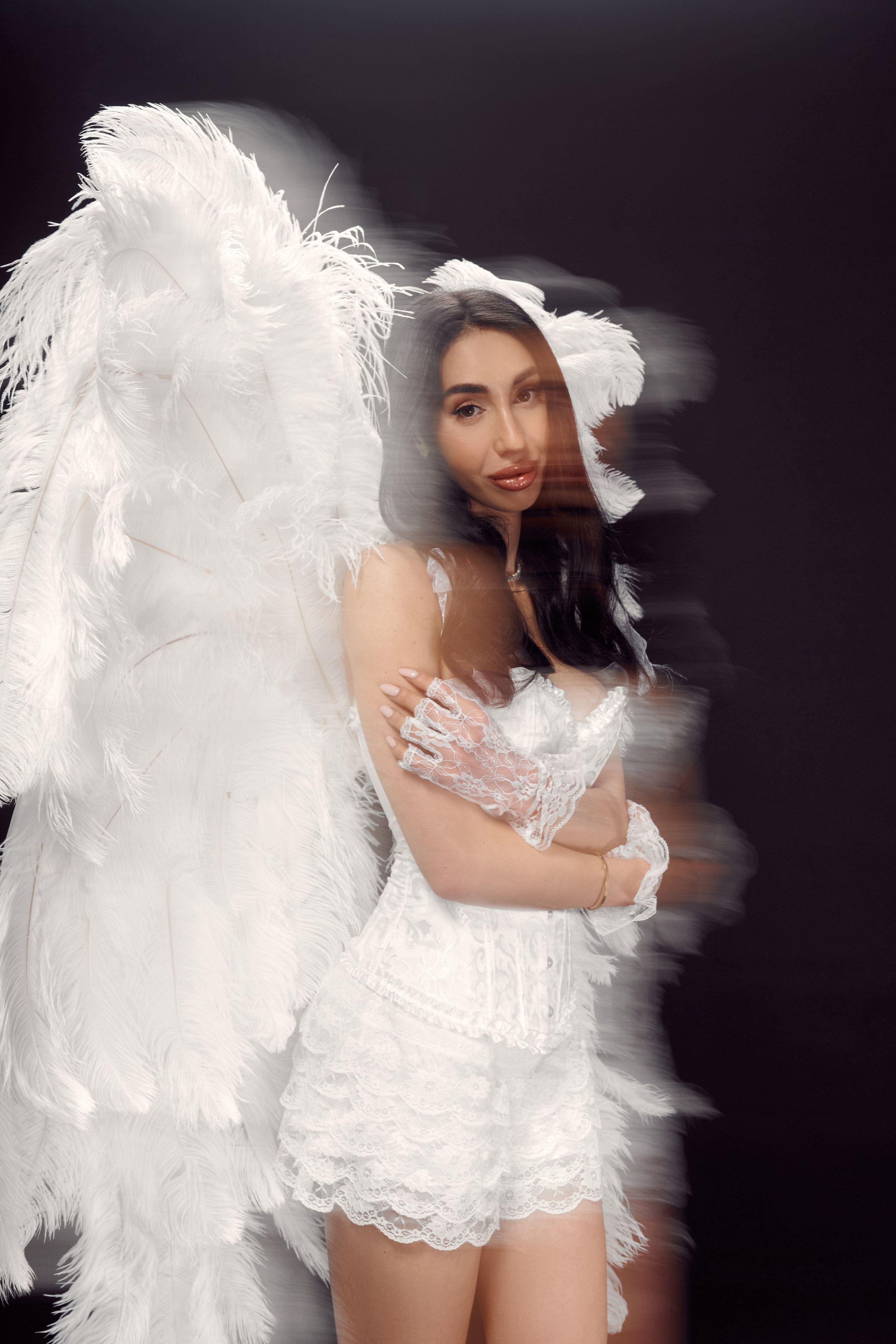 Studio portrait of blogger Ester Rogovaya with feather wings, wearing a white boudoir-style corset on a black background