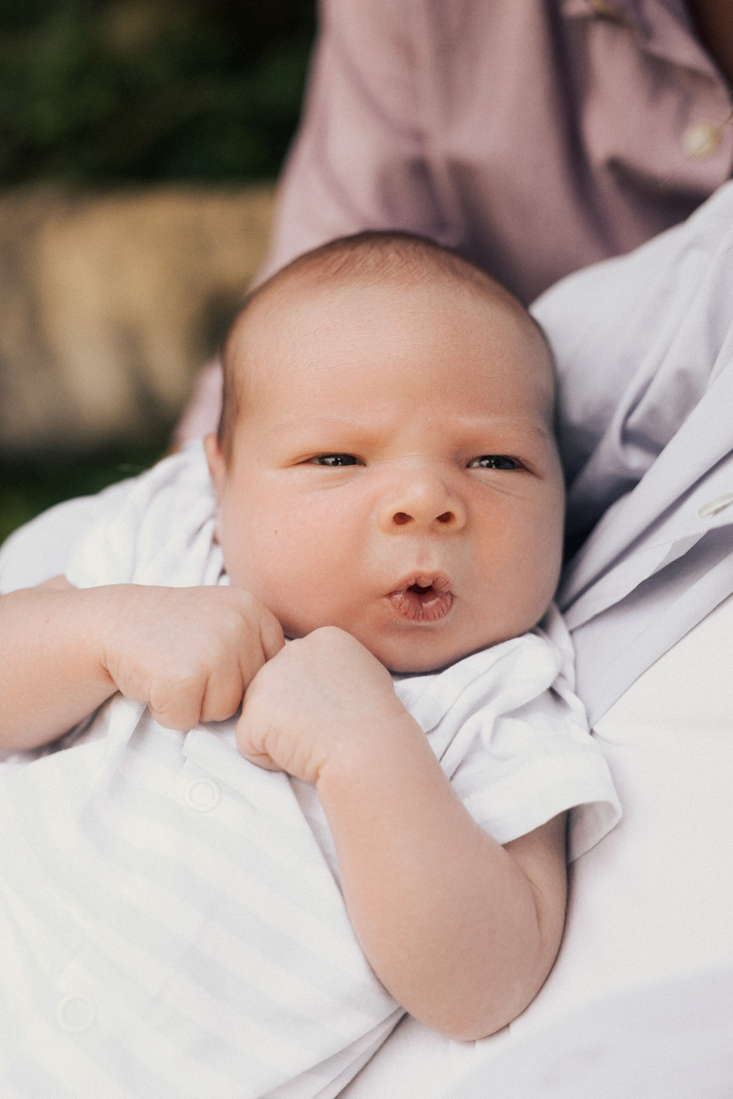 Neugeborenes Baby in weißer Kleidung liegt draußen und blickt neugierig in die Kamera – natürliche Babyfotografie in Salzburg 