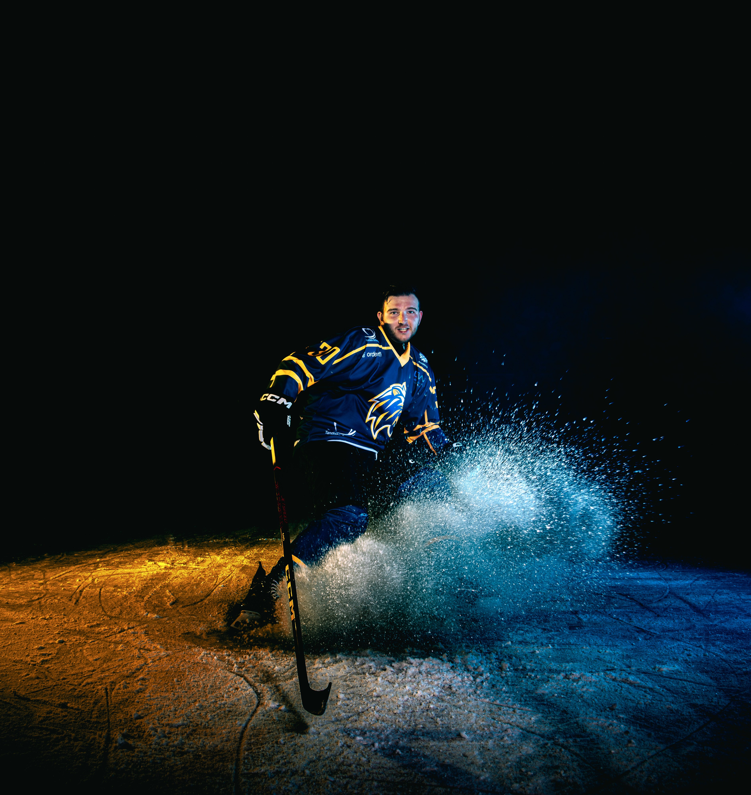 Kapture Fotografie – dramatische sportfotografie van een ijshockeyspeler in actie met krachtige belichting tijdens een ijshockeywedstrijd.