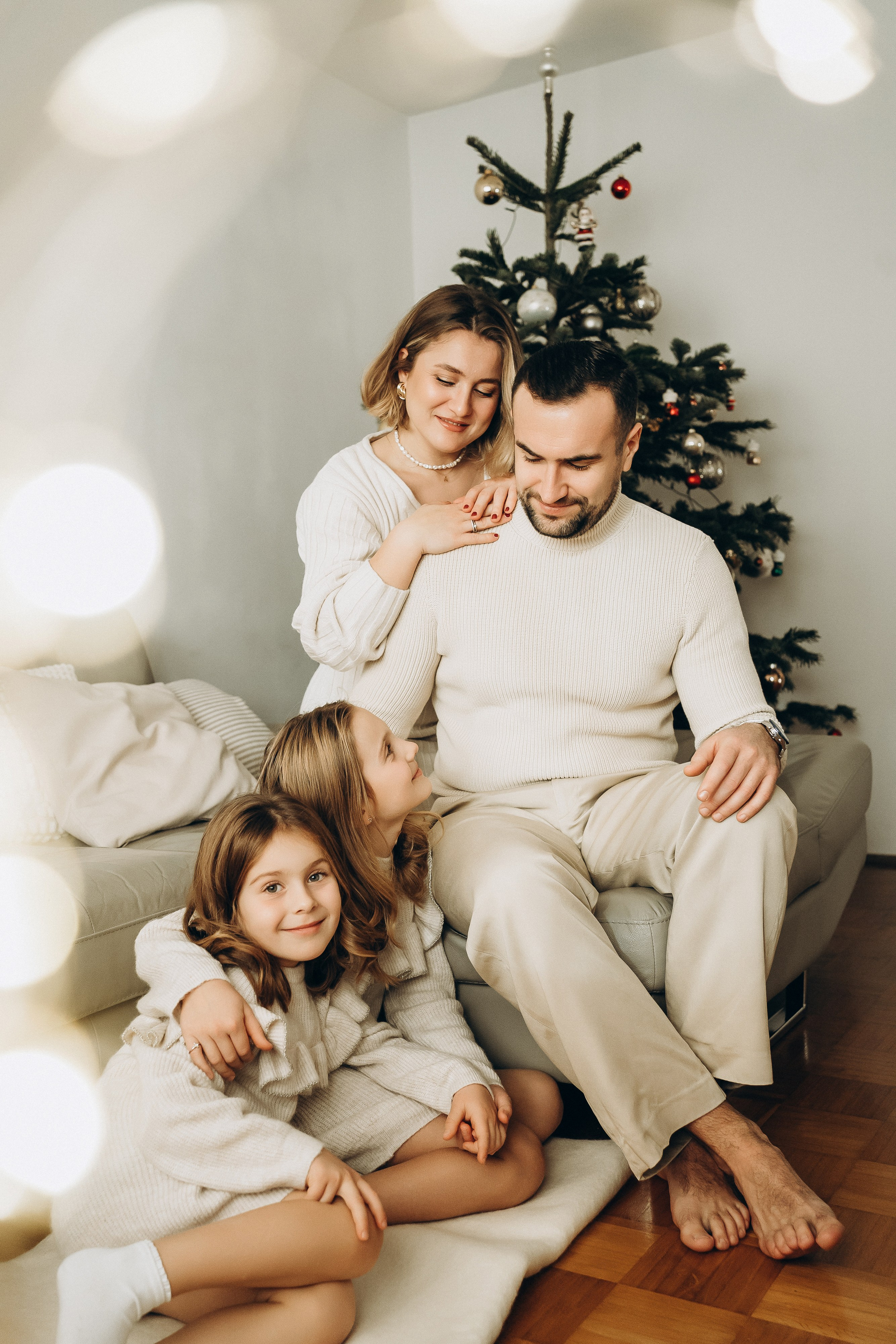 Ein herzliches Familienportrait mit allen Mitgliedern, die ihre festliche Weihnachtskleidung tragen und vor dem Weihnachtsbaum sitzen.