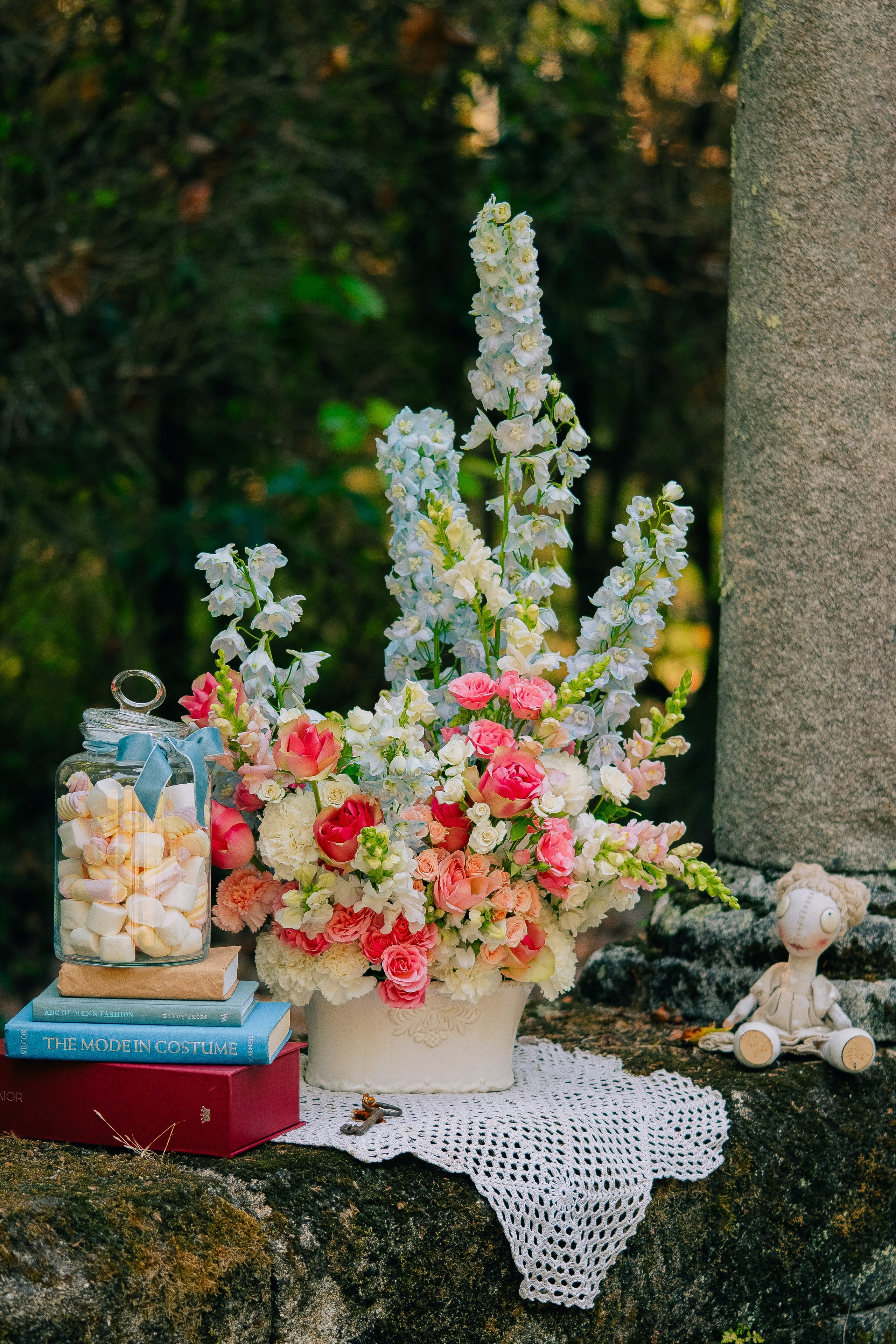 Цветочная композиция с книгами и винтажным декором. Великолепная цветочная композиция с розовыми и белыми цветами, книгами и стеклянной банкой со сладостями, расположенными на деревенской поверхности.