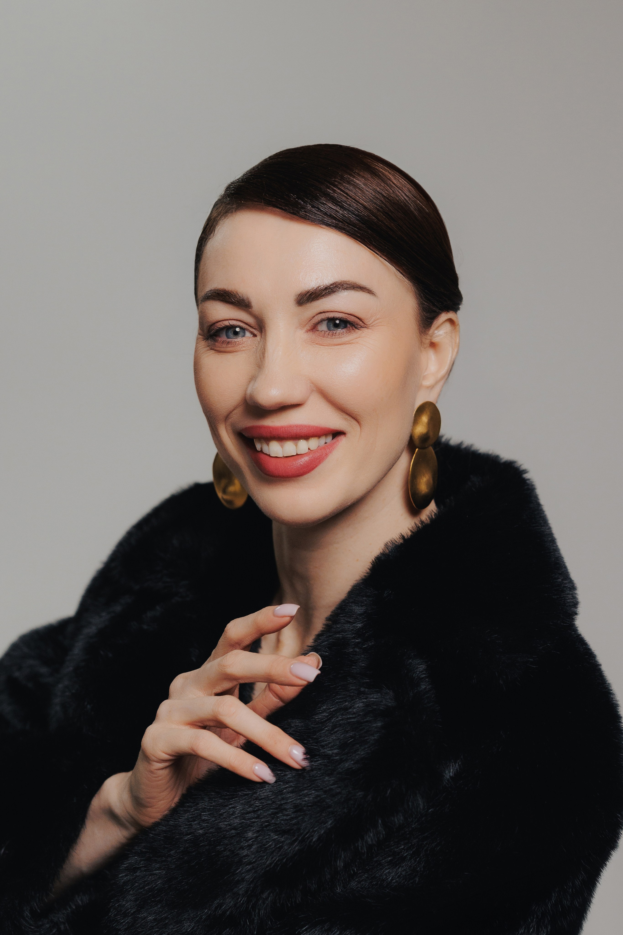Modern editorial portrait of a smiling woman in black styling photographed in a minimalist studio setting. Современный редакционный портрет улыбающейся женщины в черном образе на минималистичном студийном фоне.