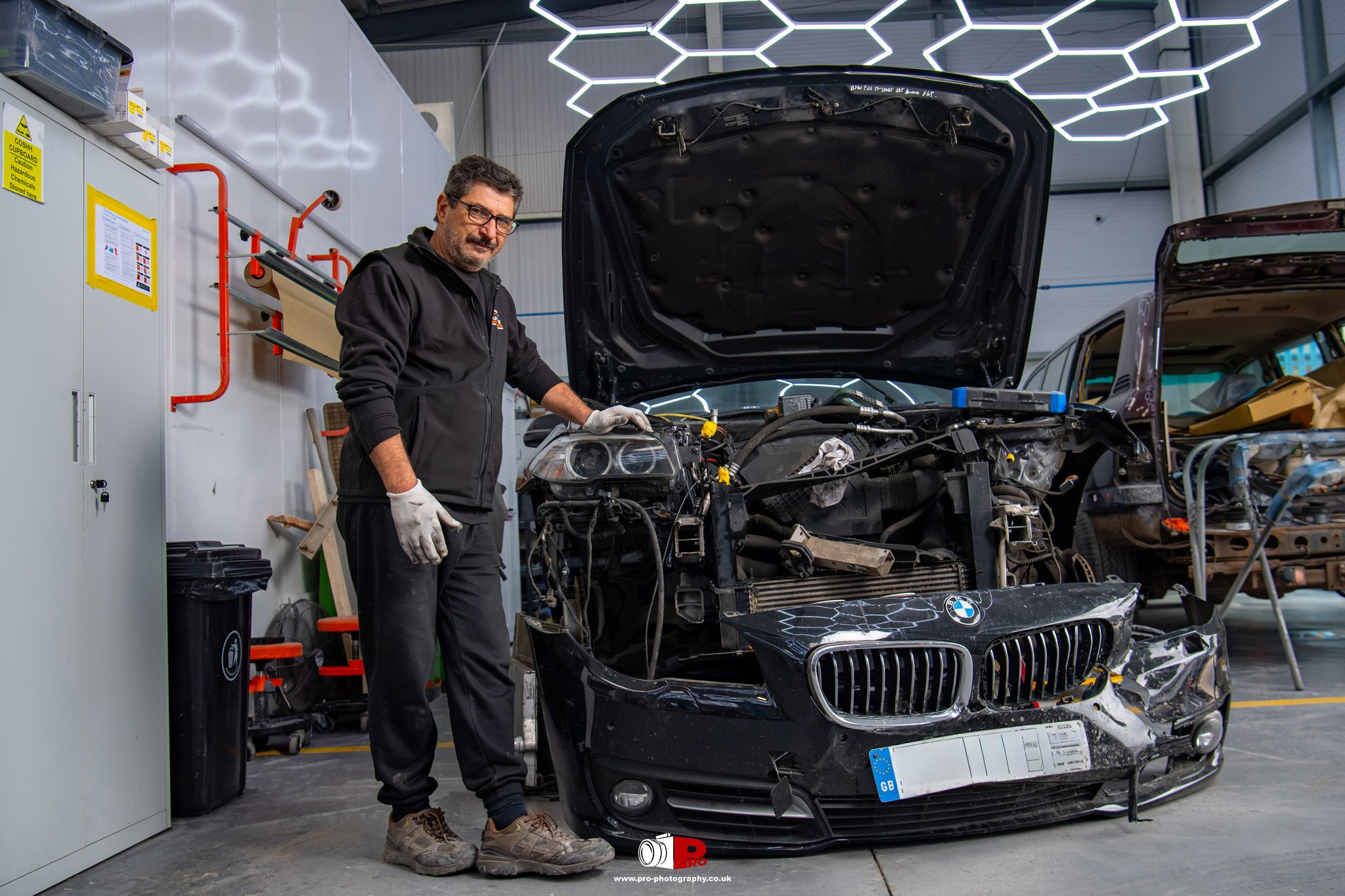 Commercial automotive image of a body repair technician standing beside a heavily damaged BMW car.