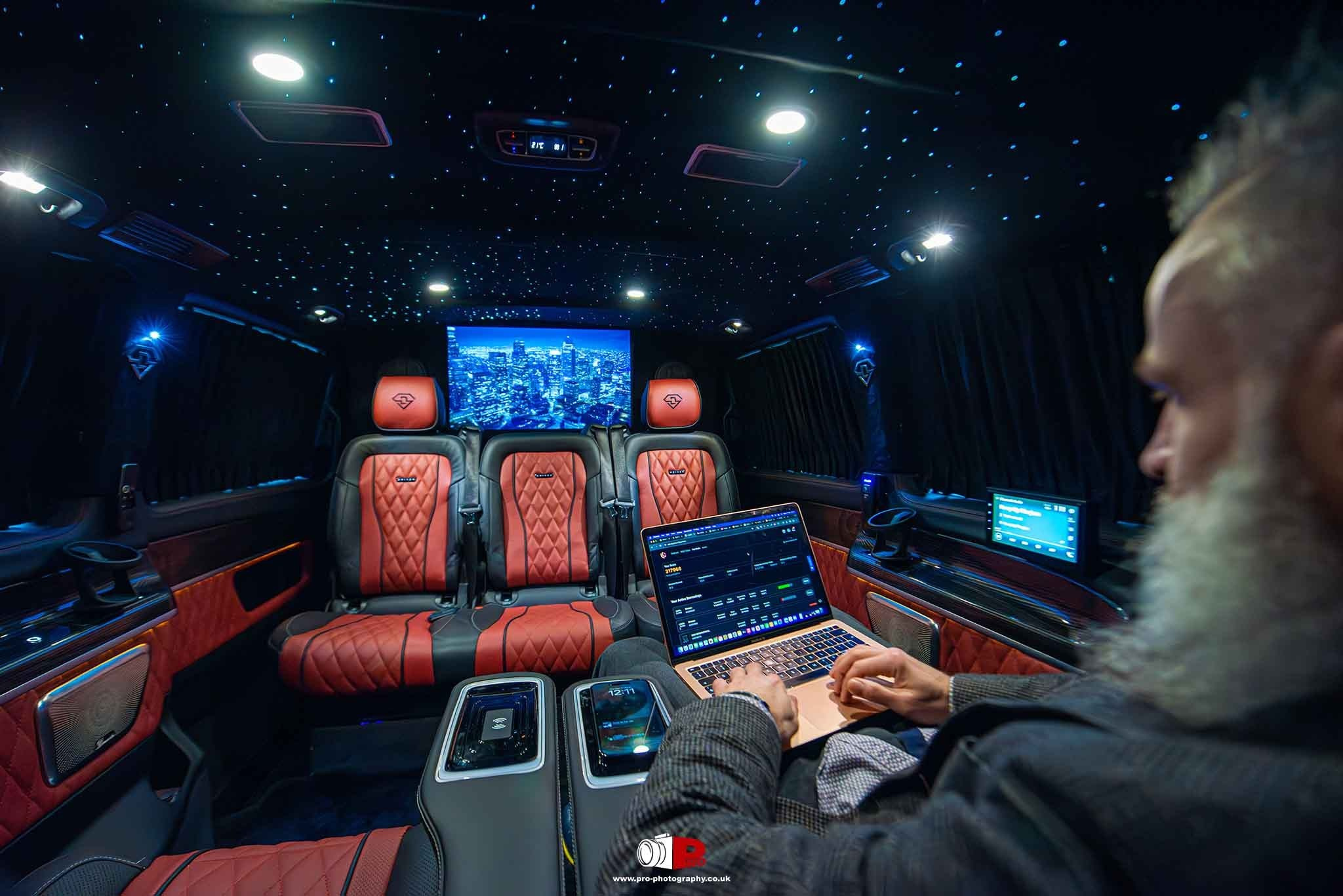 Executive van interior with red leather seating, star ceiling, screens and mobile workspace.