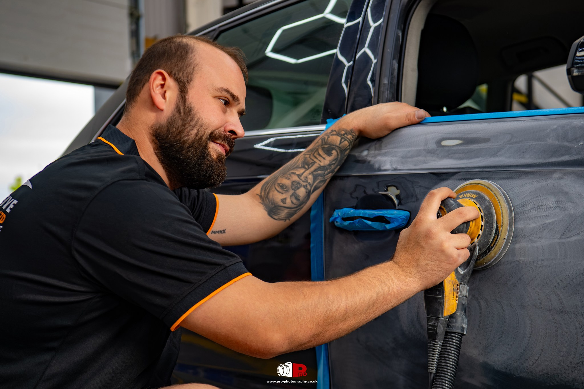 Automotive body shop technician sanding and preparing a vehicle door panel before refinishing and painting.