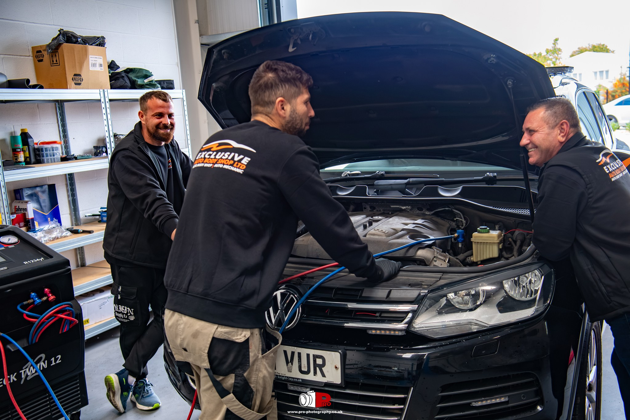 Commercial automotive image of technicians servicing a vehicle's air conditioning system inside a repair workshop.