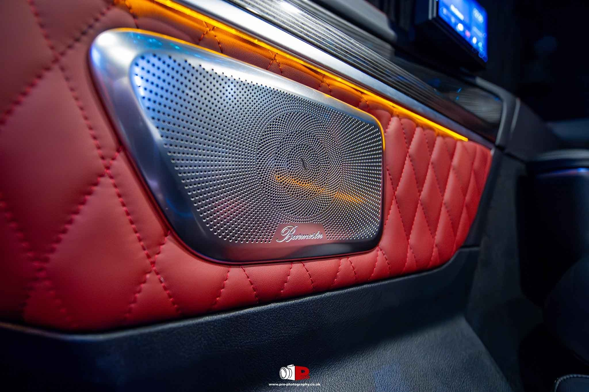 Close-up automotive detail of a Burmester speaker set into red quilted leather trim.