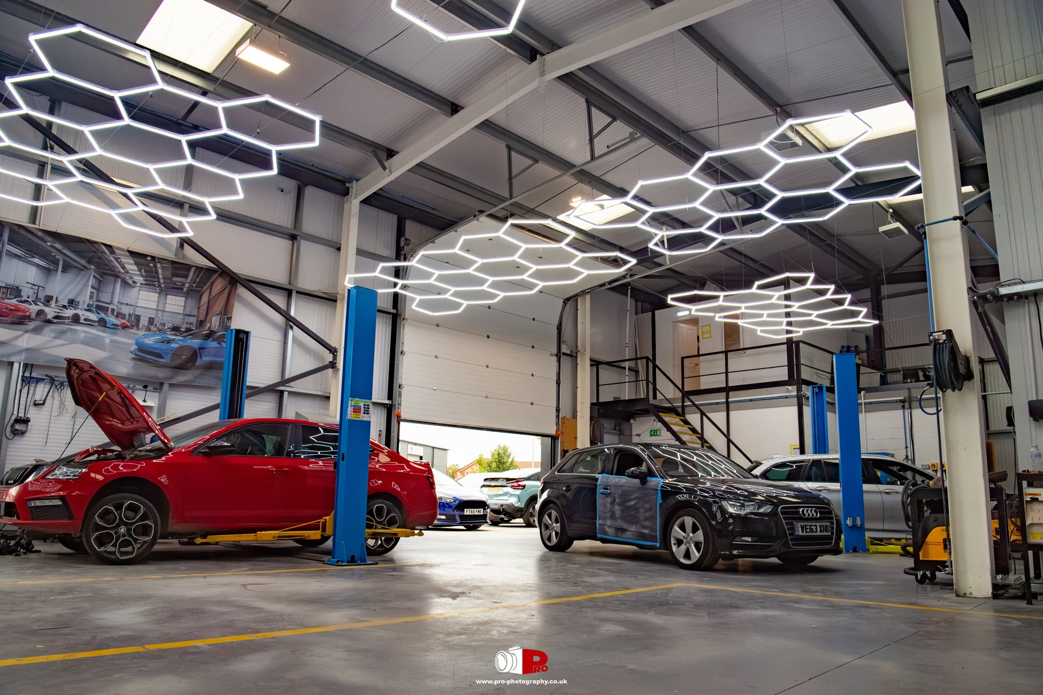 Commercial interior image of a modern automotive body repair workshop with vehicles, lifts and specialist lighting.