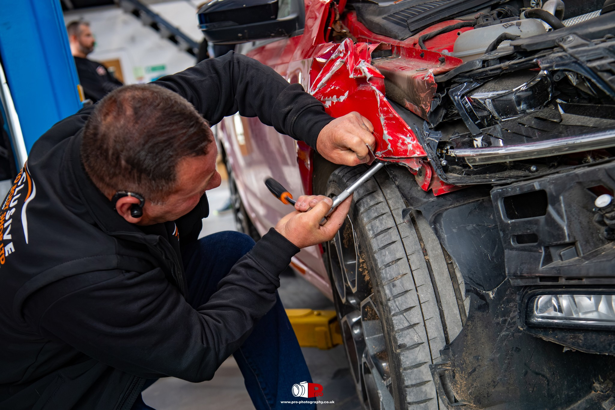 Commercial image of an automotive technician repairing accident damage to the front wing of a red car.