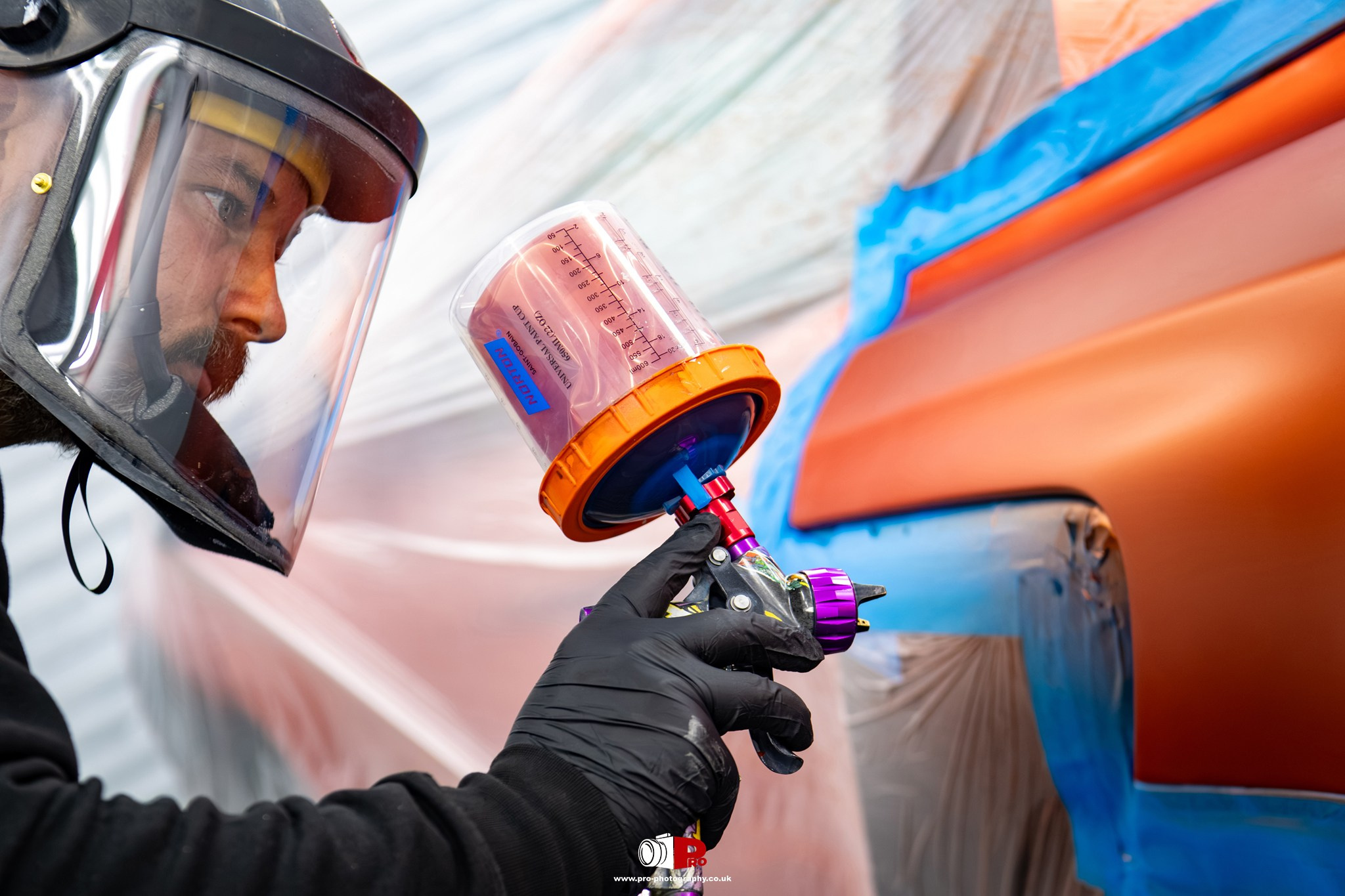 Close-up commercial image of a vehicle painter using an airbrush to apply paint inside a professional body shop.