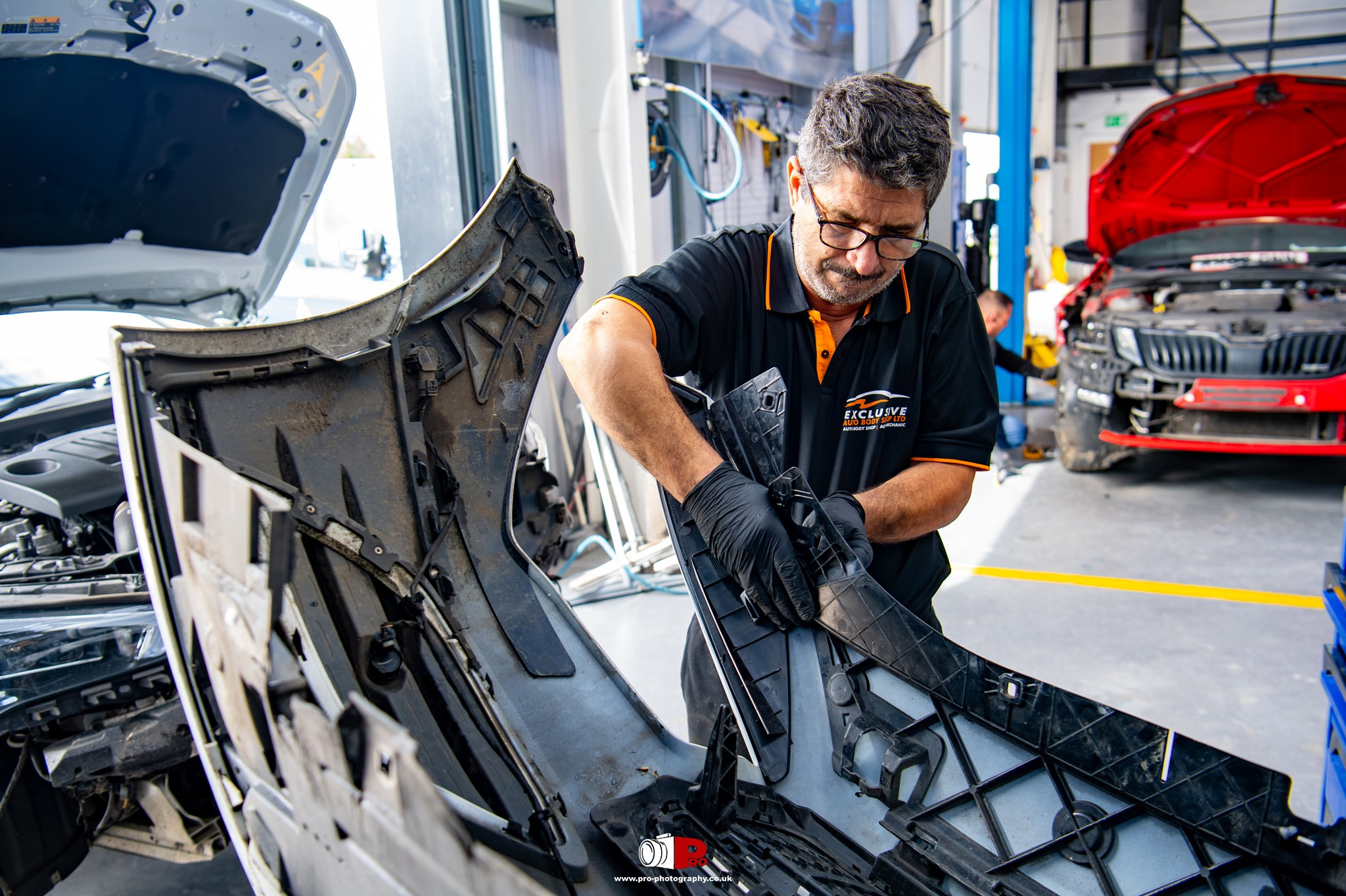 Automotive workshop image of a technician repairing and refitting a vehicle bumper during bodywork restoration.