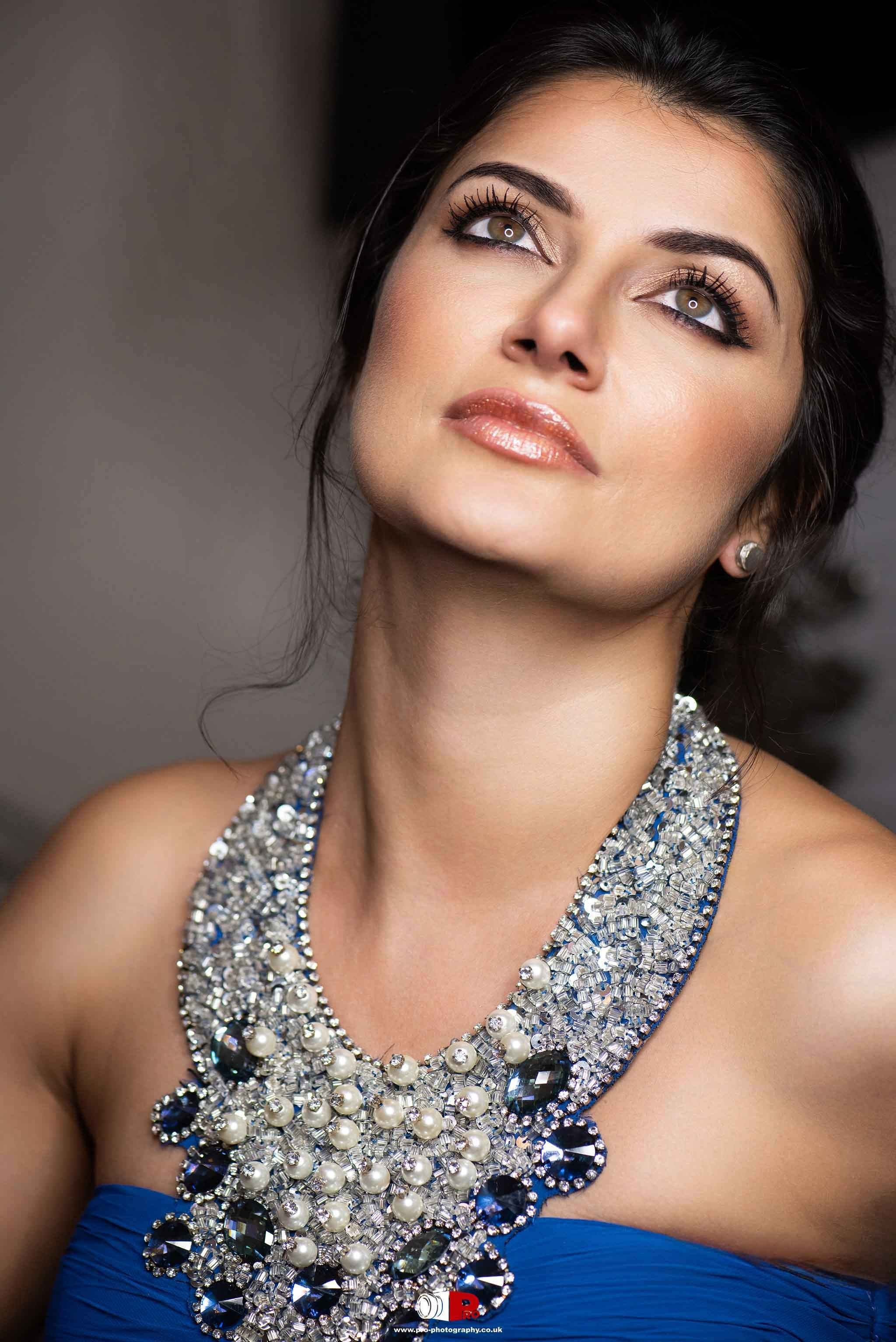 Close-up beauty portrait with elegant makeup, dark hair and a statement jewelled necklace.