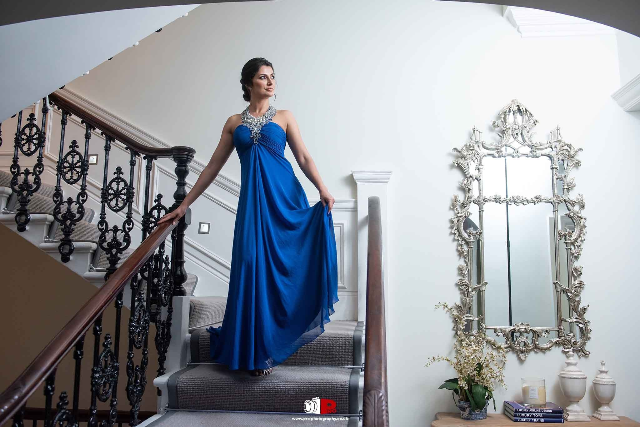 Fashion portrait of a woman in an elegant blue gown on a grand staircase.
