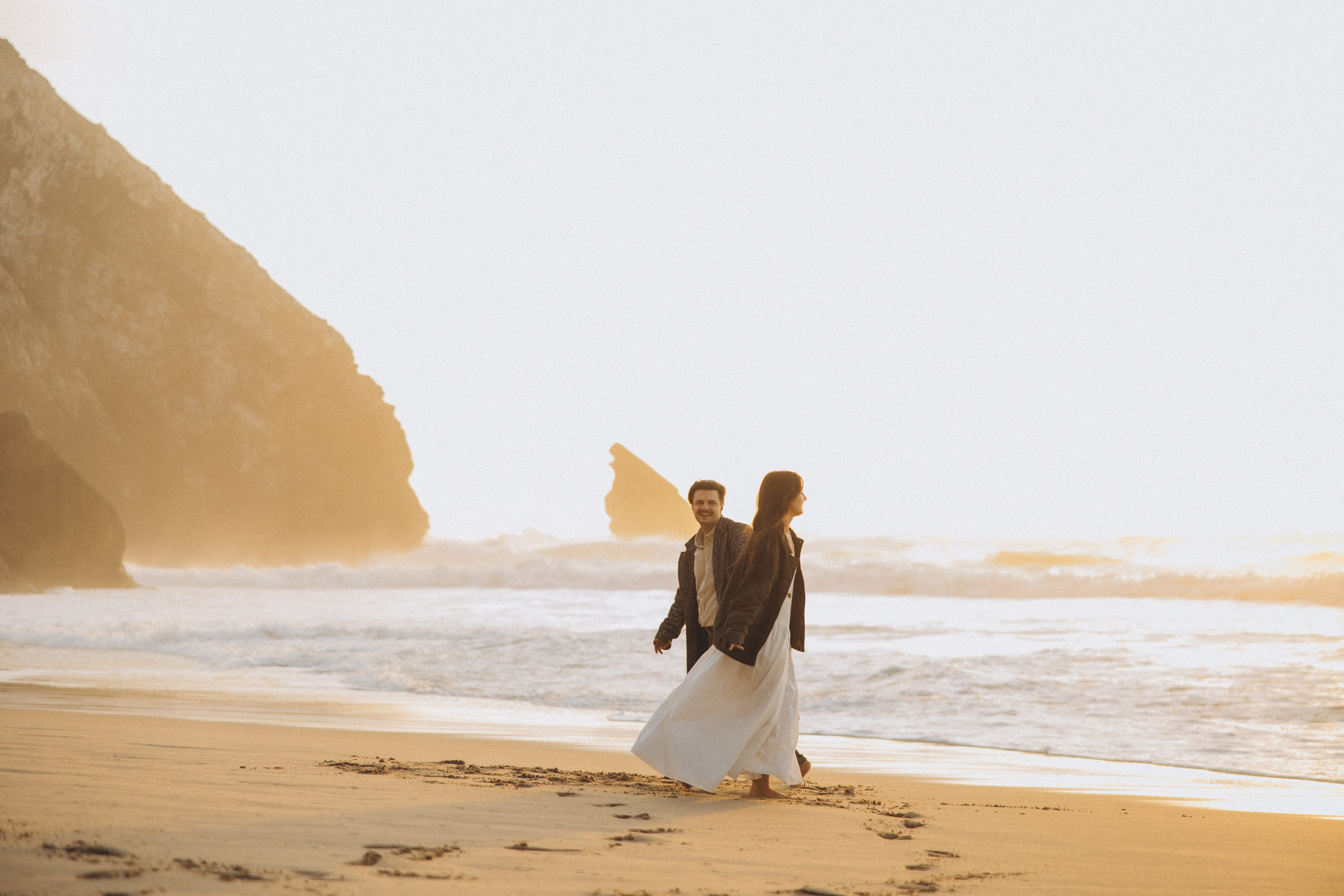 Couple holding hands and walking through a picturesque coastline in Portugal.
